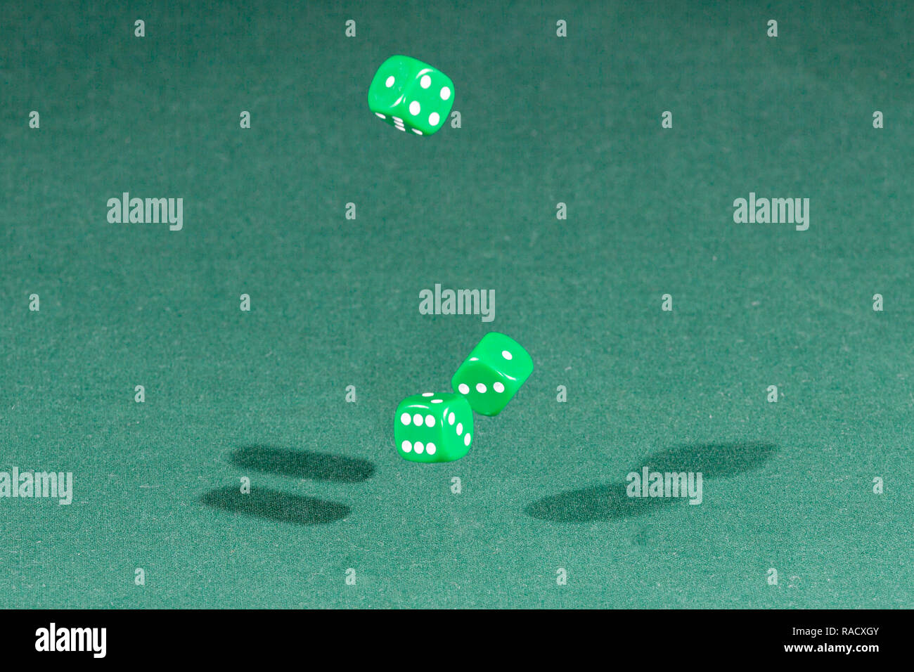 Three green dices falling on a green table Stock Photo