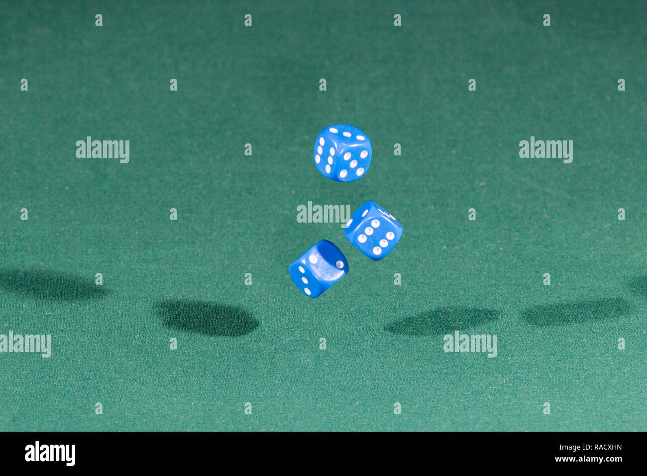 Three blue dices falling on a green table Stock Photo