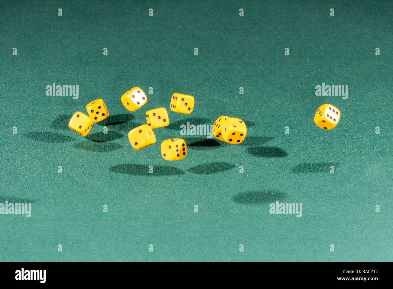 Ten yellow dices falling on a green table Stock Photo