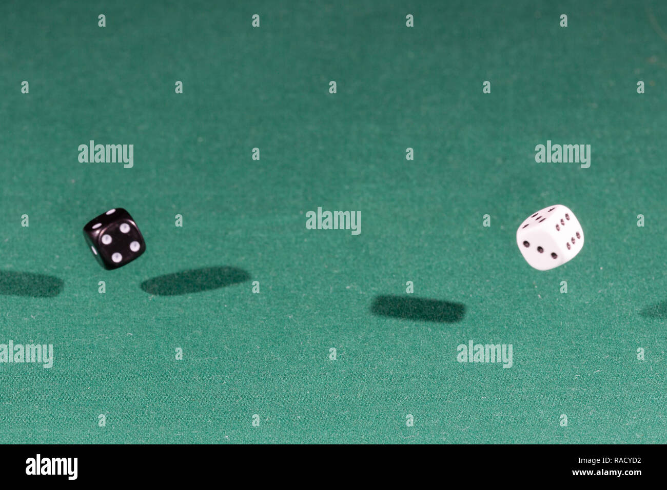 Two white and black dices falling on a green table Stock Photo