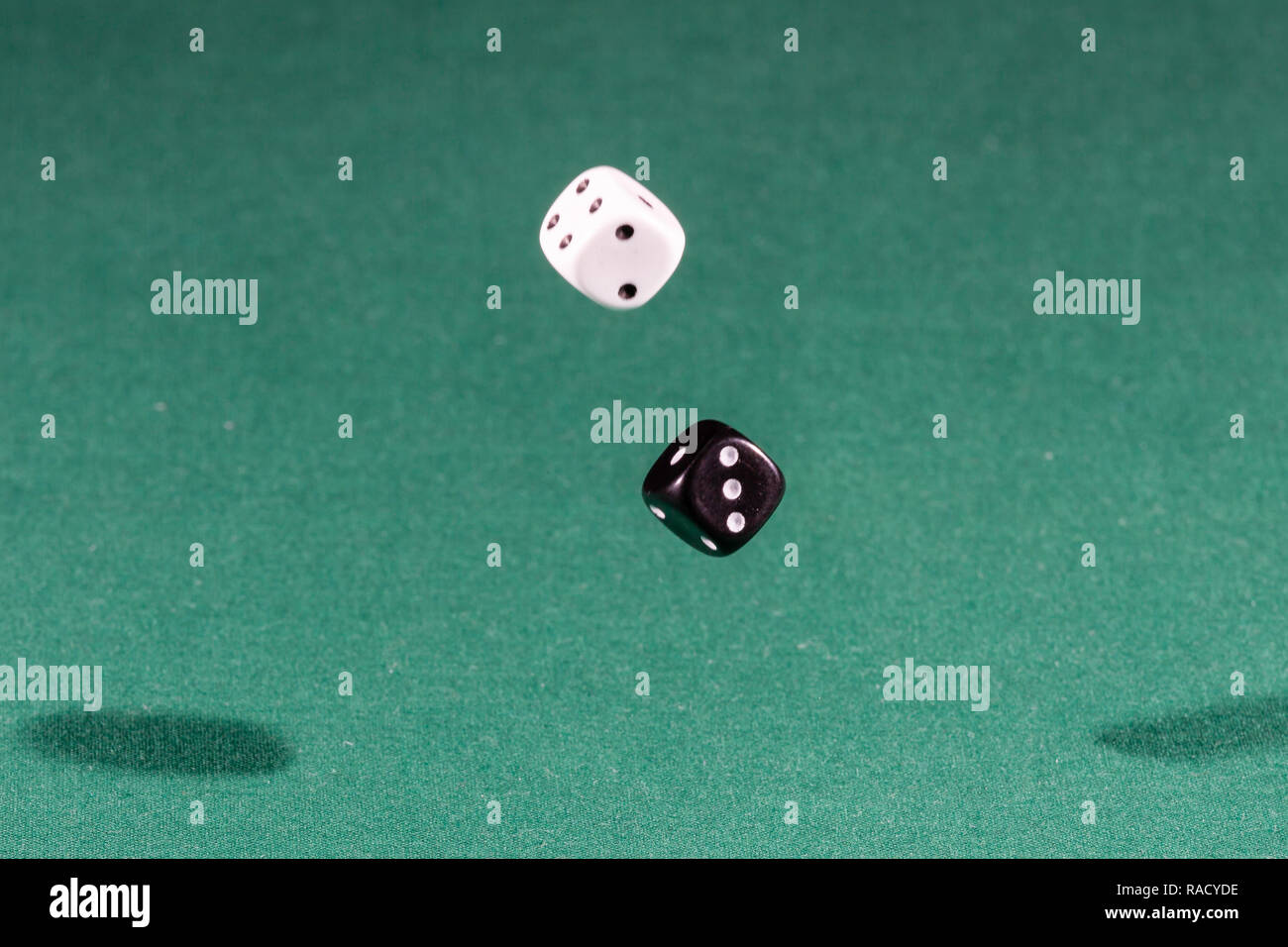 Two white and black dices falling on a green table Stock Photo