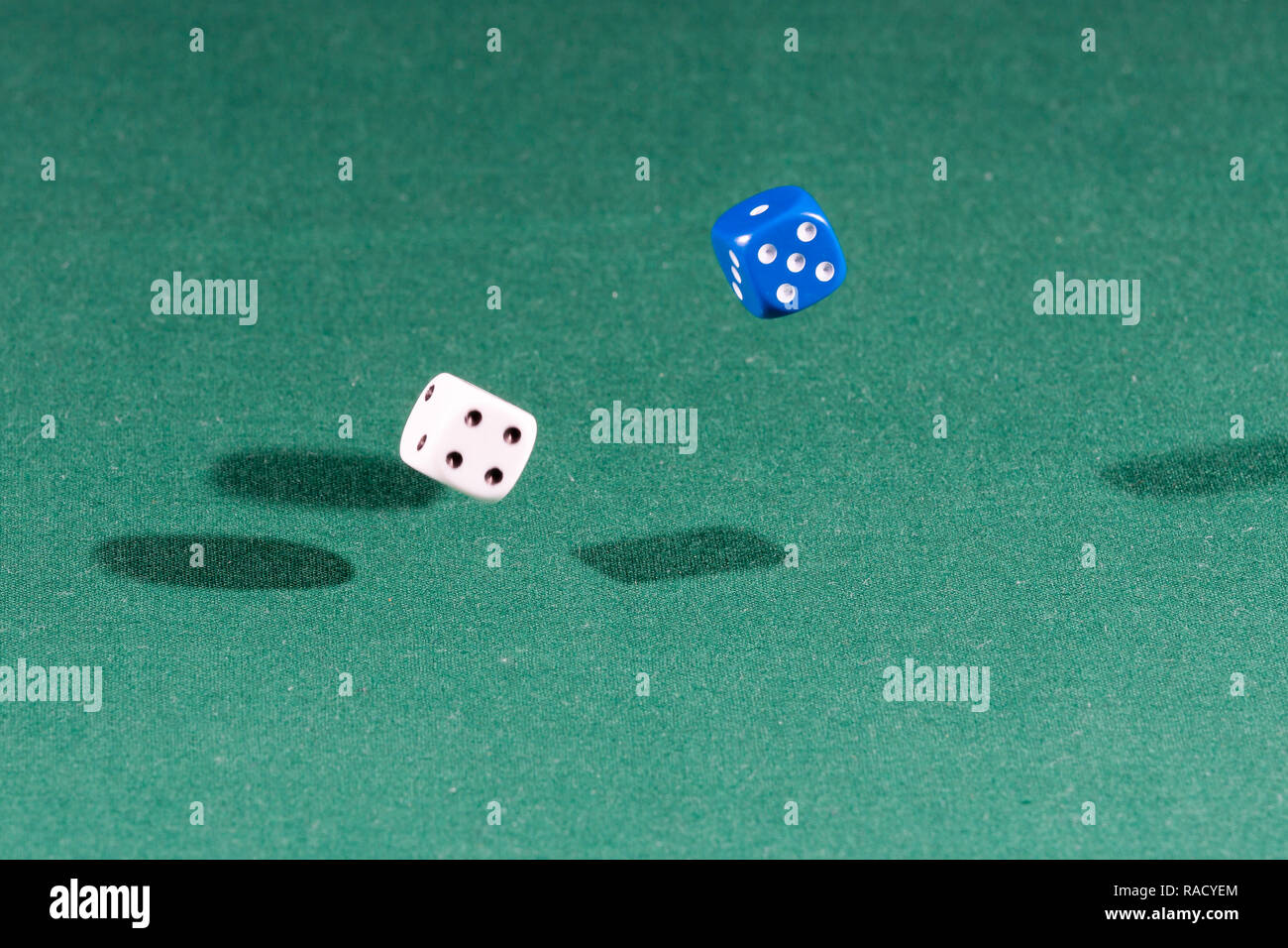 Two white and blue dices falling on a green table Stock Photo