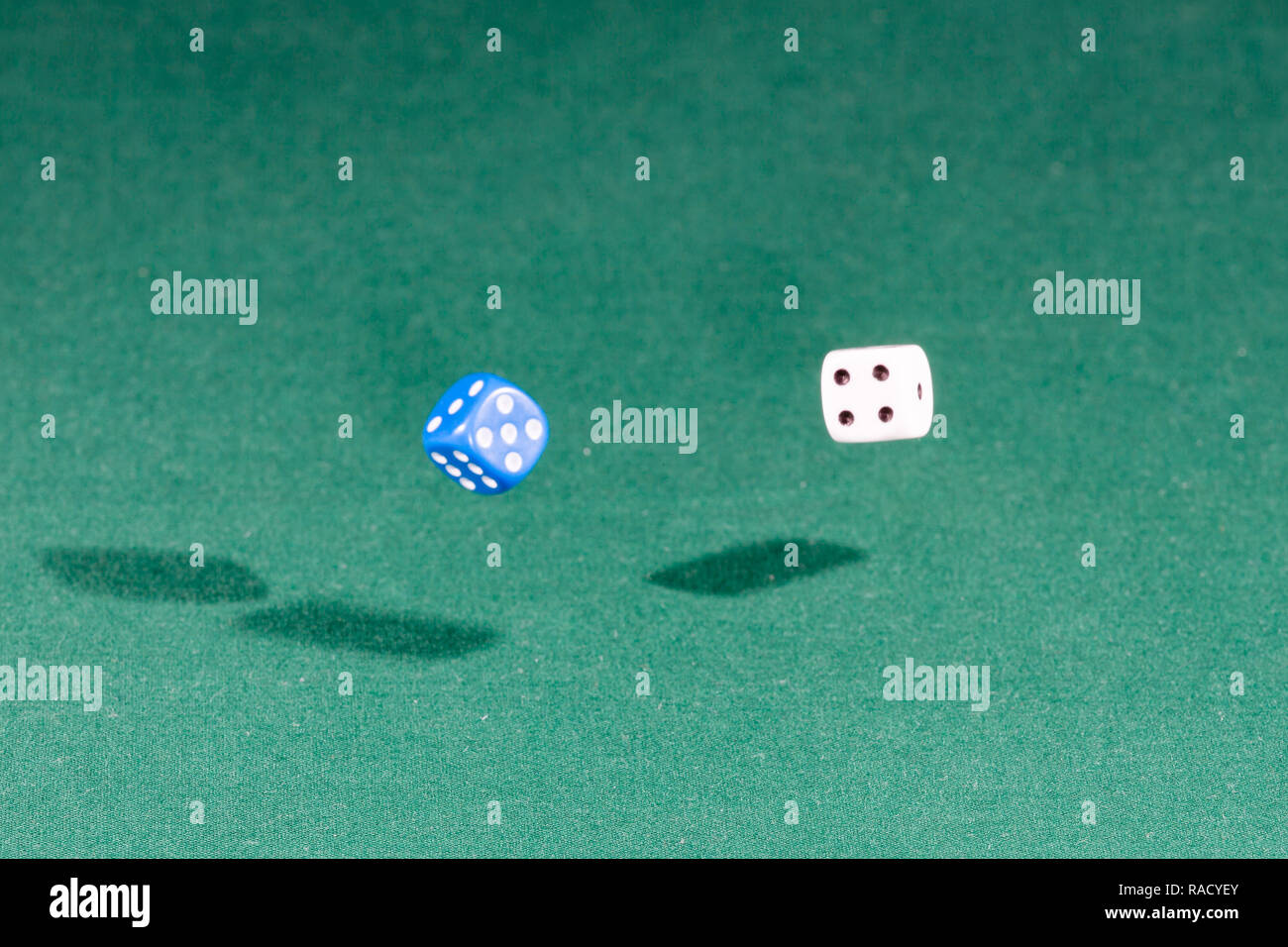 Two white and blue dices falling on a green table Stock Photo