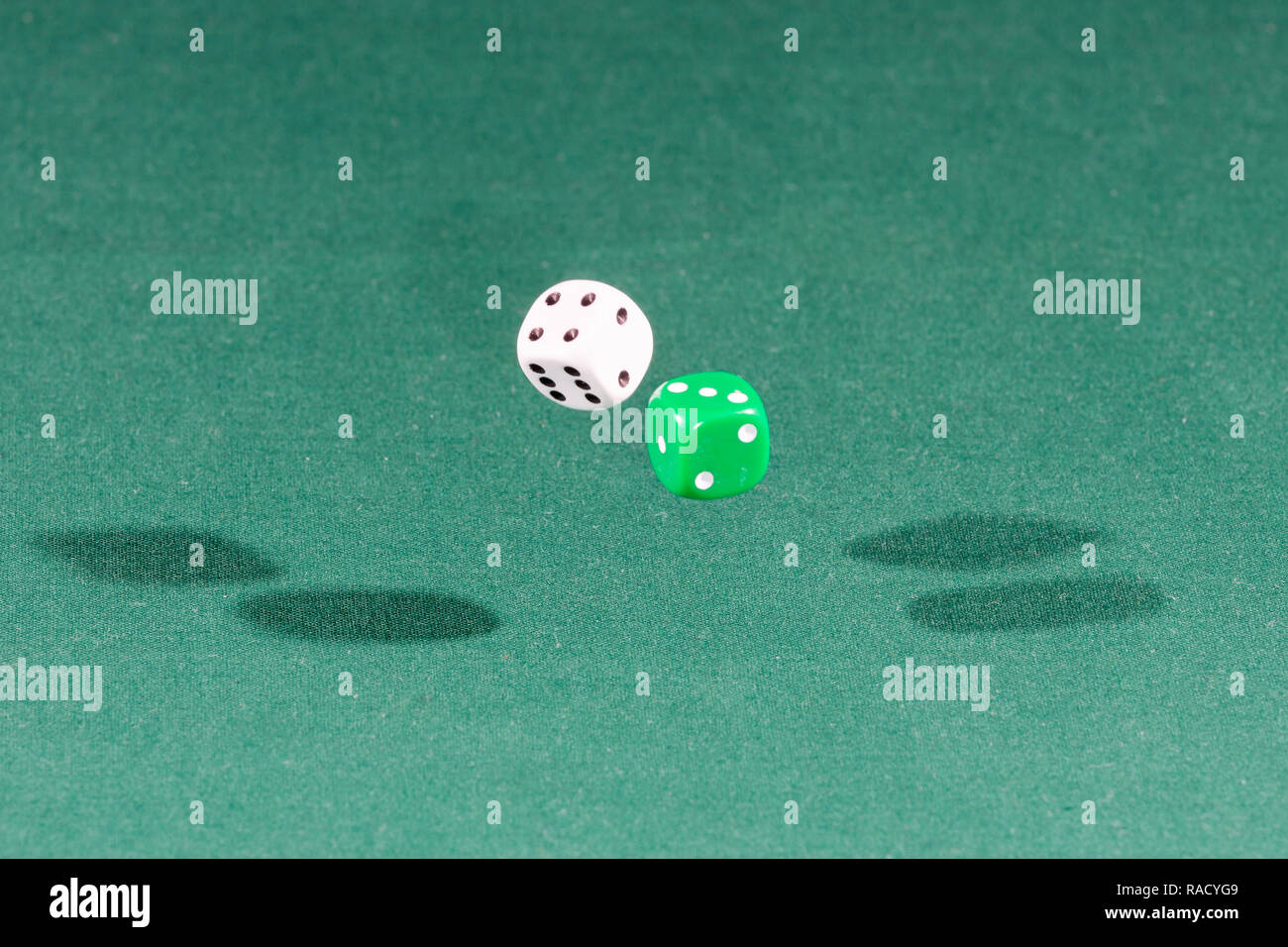 Two white and green dices falling on a green table Stock Photo