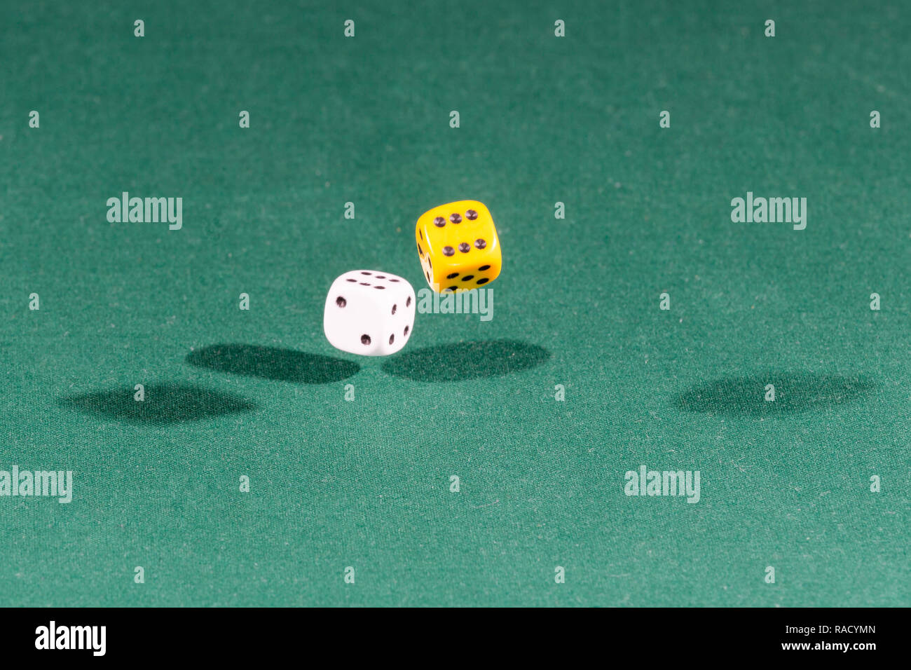 Two white and yellow dices falling on a green table Stock Photo