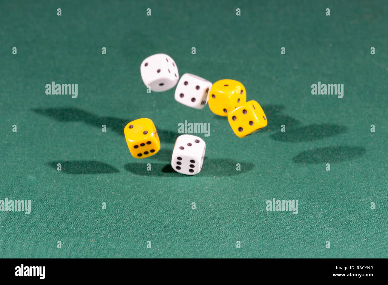 Six white and yellow dices falling on a green table Stock Photo