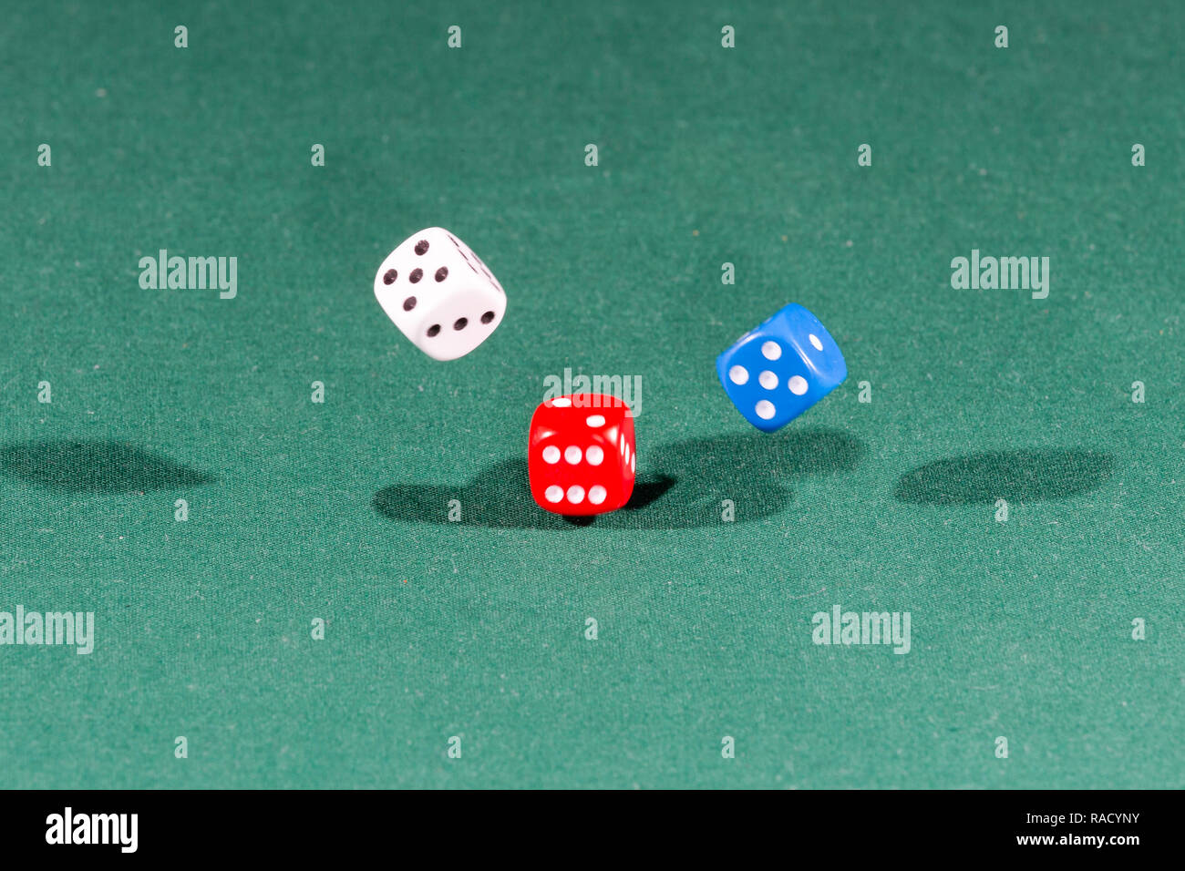 White, red and blue dices falling on a green table Stock Photo