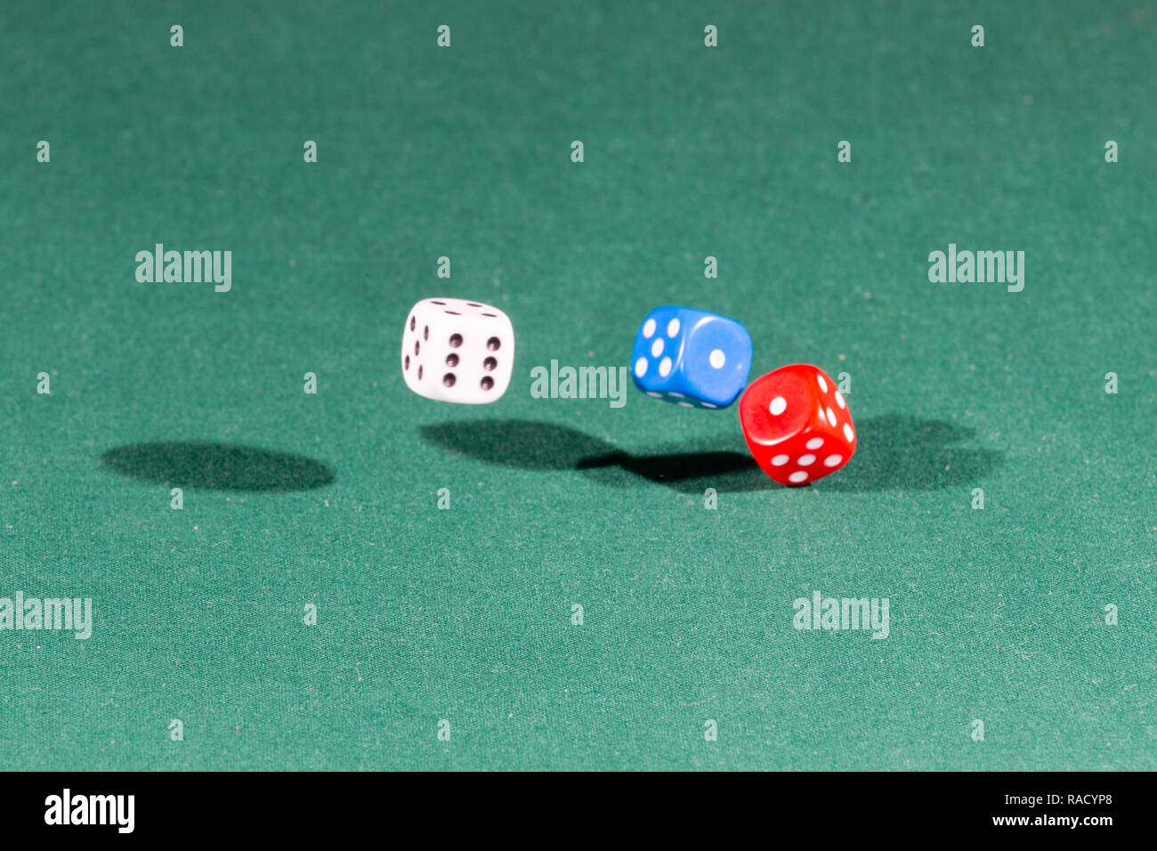 White, red and blue dices falling on a green table Stock Photo