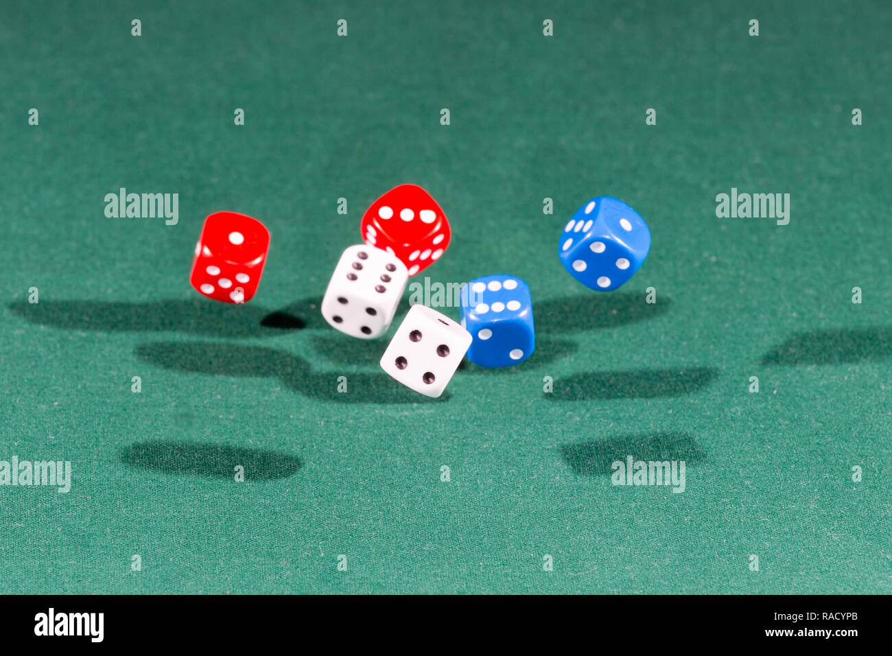 White, red and blue dices falling on a green table Stock Photo