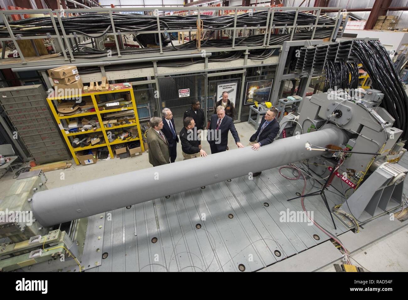 DAHLGREN (Jan. 12, 2017) Tom Boucher, second from right, program manager for the Electromagnetic Railgun at the Office of Naval Research (ONR), talks to Rear Adm. David Hahn, chief of naval research, during a visit to the railgun facility located at Naval Surface Warfare Center, Dahlgren Division. The EM Railgun launcher is a long-range weapon that fires projectiles using electricity instead of chemical propellants. Magnetic fields created by high electrical currents accelerate a sliding metal conductor, or armature, between two rails to launch projectiles at 4,500 mph. Stock Photo