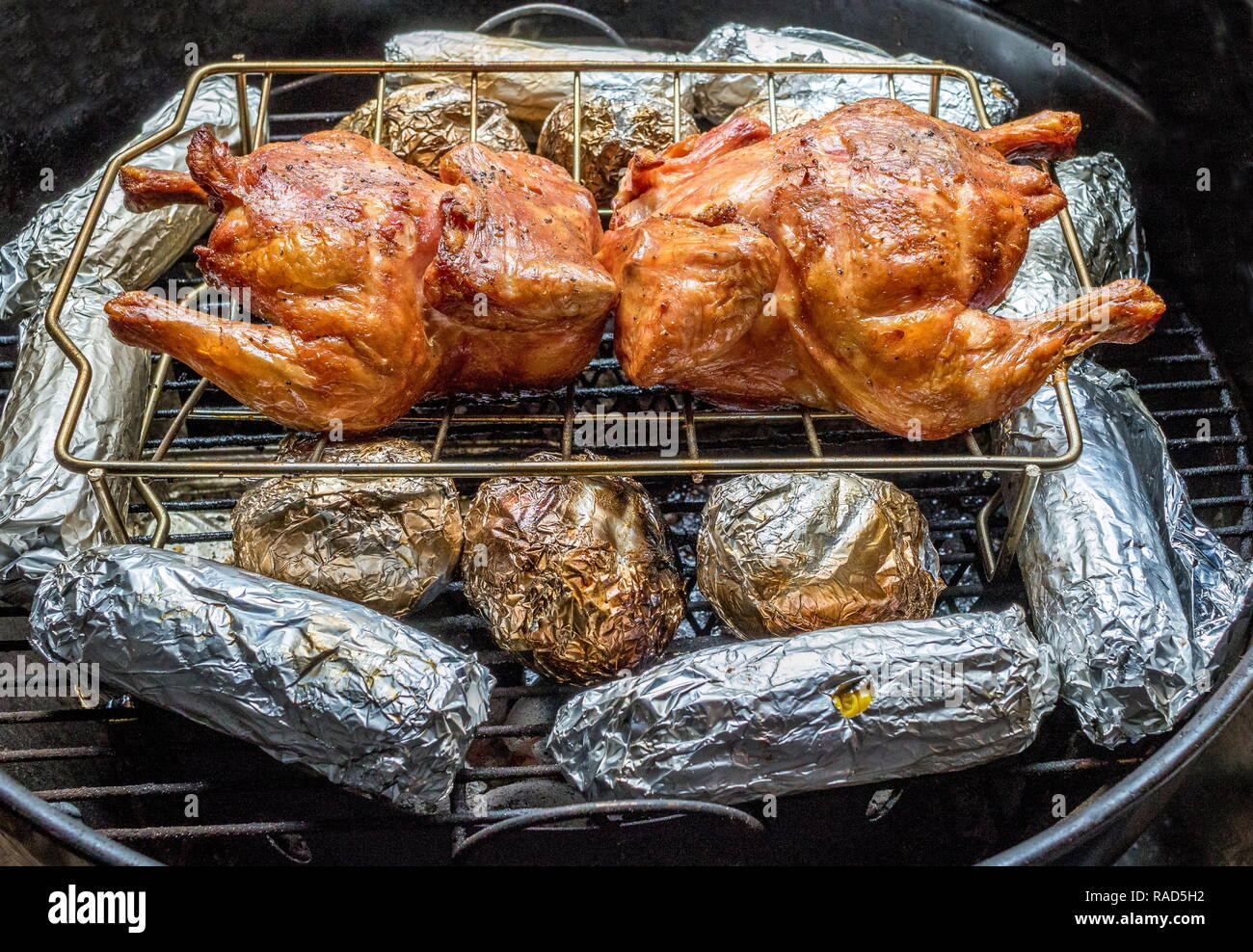 Roasted chickens and foil wrapped potatoes and corn in an outdoor