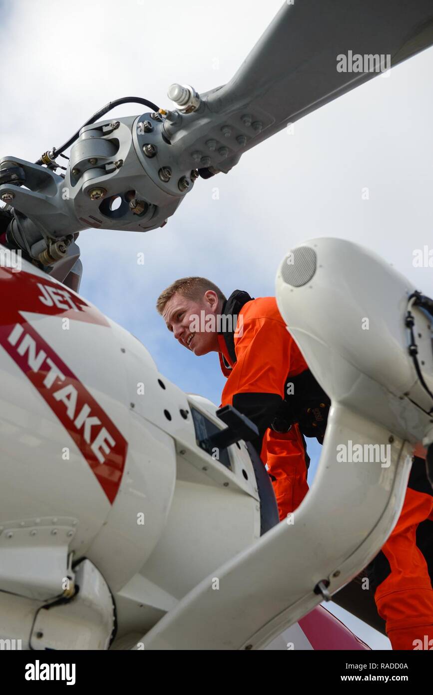 Coast Guard Lt. Nicholas Peters inspects the rotor head and anti-icing sensor before turning on the engines of the MH-60 Jayhawk helicopter at Air Station Cape Cod in Massachusetts, Jan. 19, 2017. The anti-ice and de-icing systems are activated when ice accumulates on the engines and rotor blades of the helicopter. Stock Photo