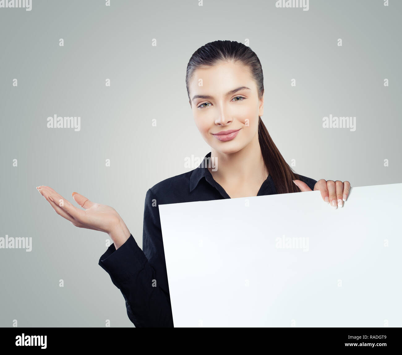 Cute business woman with empty open hand and white blank paper banner background. Young woman smiling. Business and education concept Stock Photo