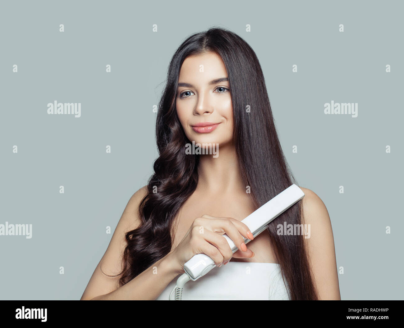 Beautiful woman with long straight hair and curly hair using hair straightener. Cute smiling girl straightening healthy brunette hairstyle with flat i Stock Photo
