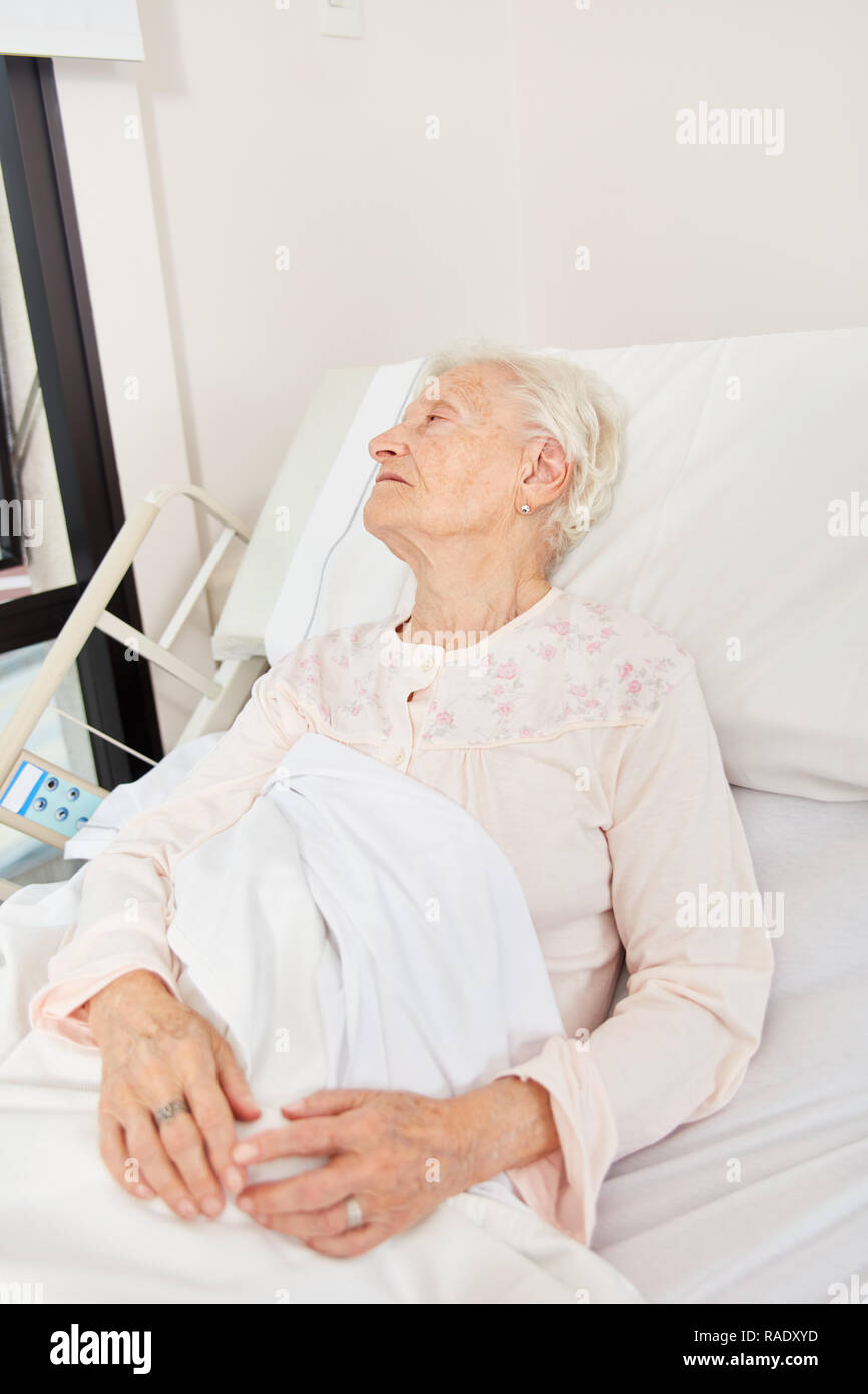 Senior woman lying weak and ill in bed in nursing home or hospital