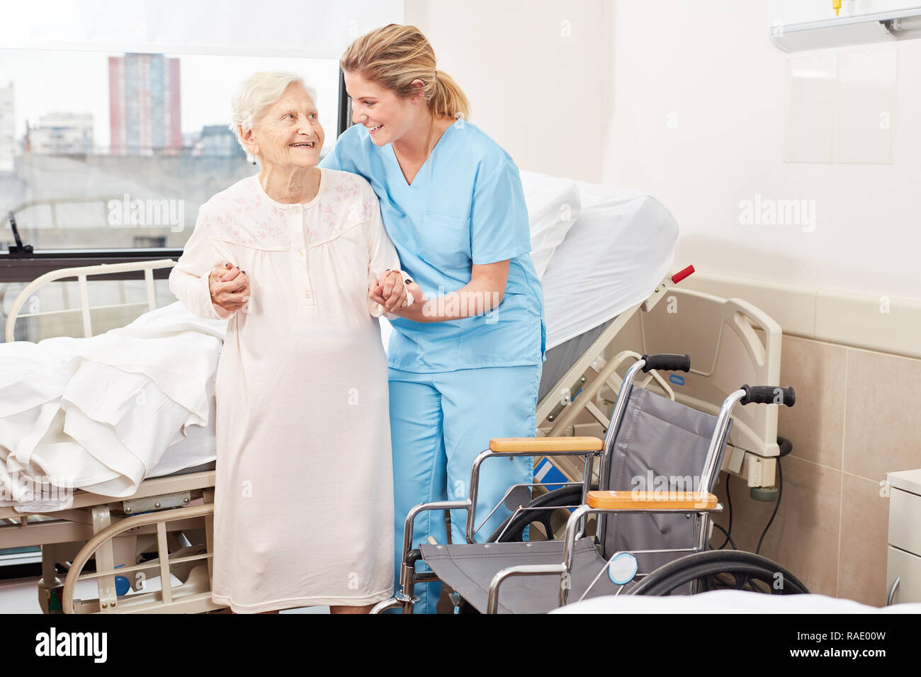 Nursing lady helps frail elderly woman to wheelchair at the hospital