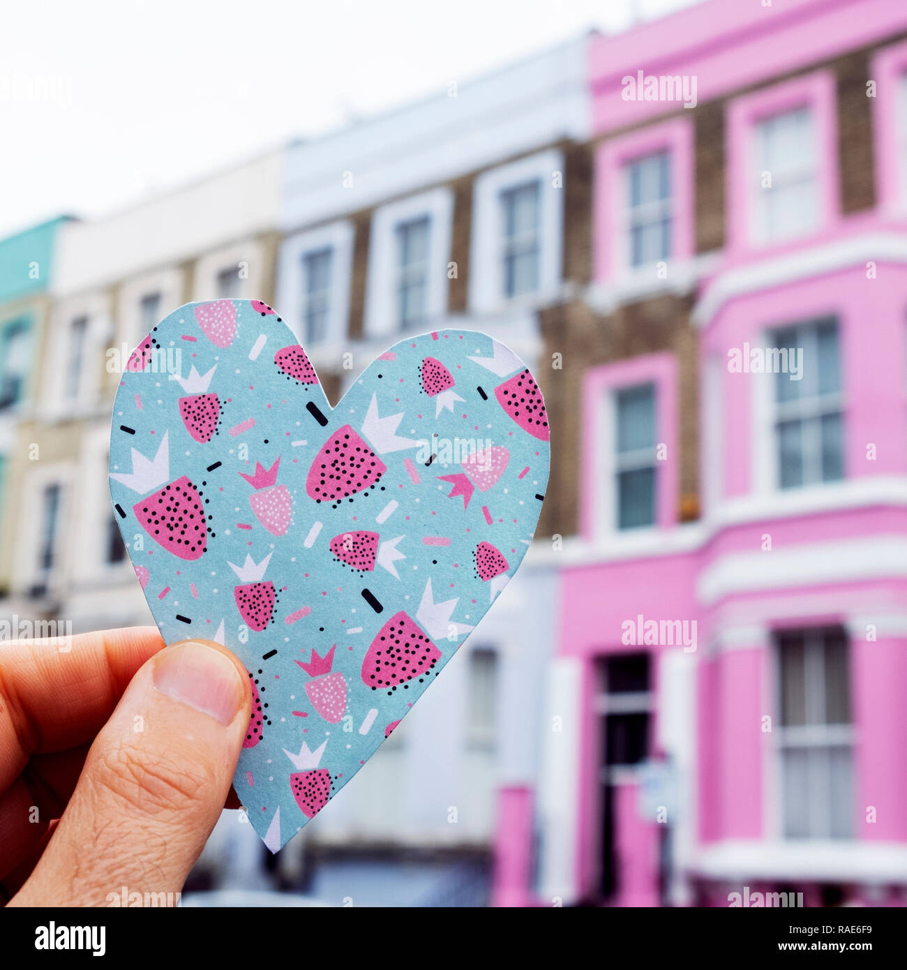 closeup of a caucasian man holding a heart cutout on a colorful paper, in front of a row of colorful houses in the popular portobello road in london,  Stock Photo