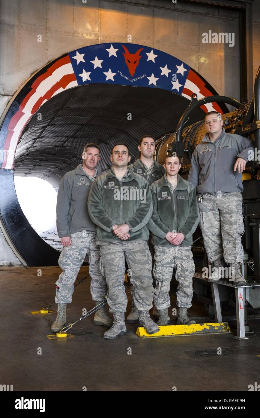 Air National Guardsmen from New Jersey's 177th Fighter Wing, “Jersey Devils”, pose for a photo in front of the morale painting they designed, funded and created at their unit’s engine test cell facility, located at the Atlantic City Air National Guard Base, N.J., on Jan. 31, 2017. The propulsion shop personnel, including two members not shown, wanted to create a feeling of Esprit de Corps and a reminder of just how amazing it is to work on such a complex and important military machine. The General Electric F110-GE-100 turbofan, prepped and ready for testing, produces close to 29,000 pounds of  Stock Photo