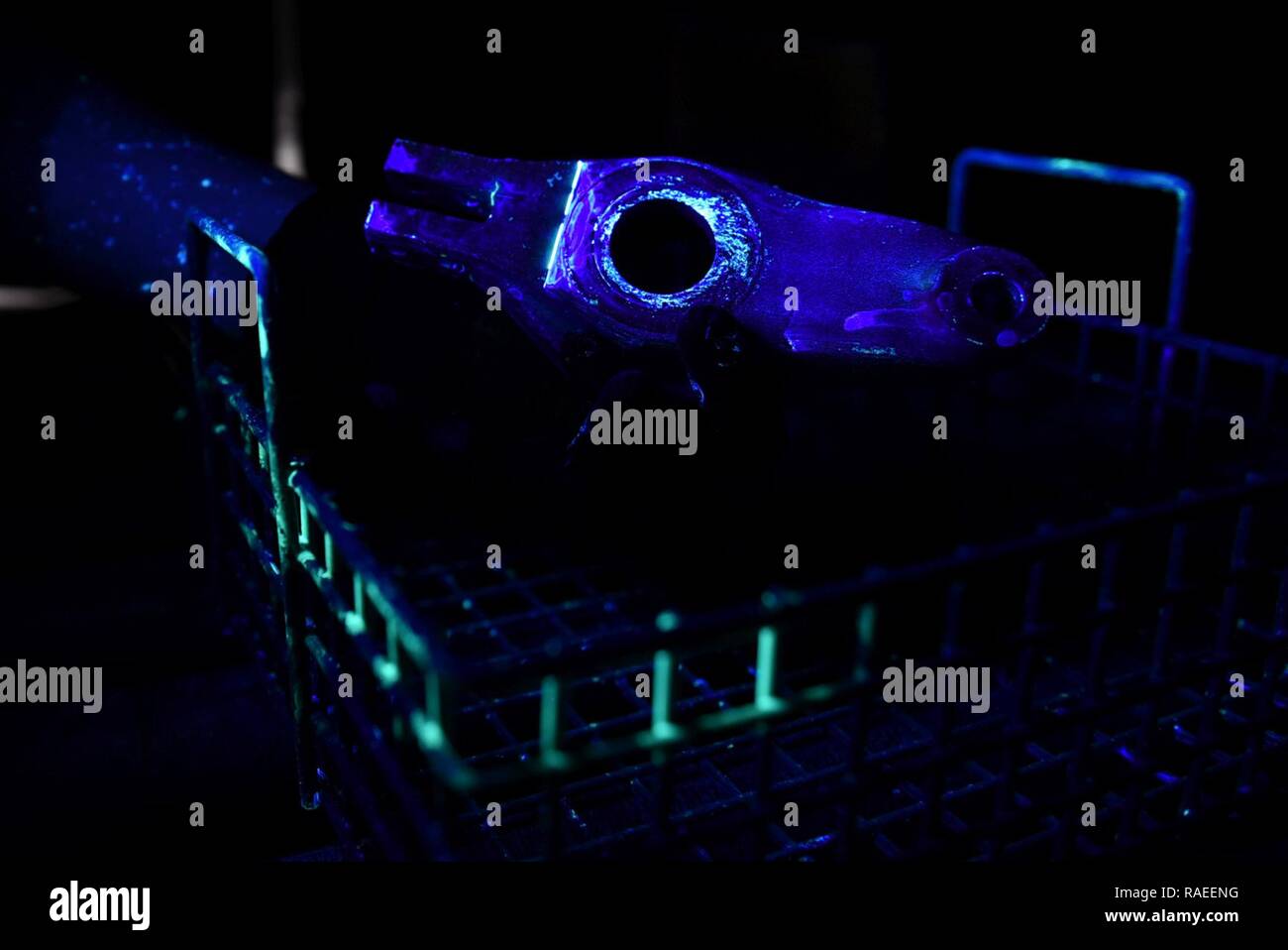 U.S. Air Force Airman 1st Class James Schwein, 19th Maintenance Squadron nondestructive inspections journeyman, uses a black light to inspect an aircraft tow fitting arm for cracks Jan. 19, 2017, at Little Rock Air Force Base, Ark. Liquid penetrant fills in small cracks causing them to become fluorescent under black lighting, making it easier to detect cracks and corrosion. Stock Photo