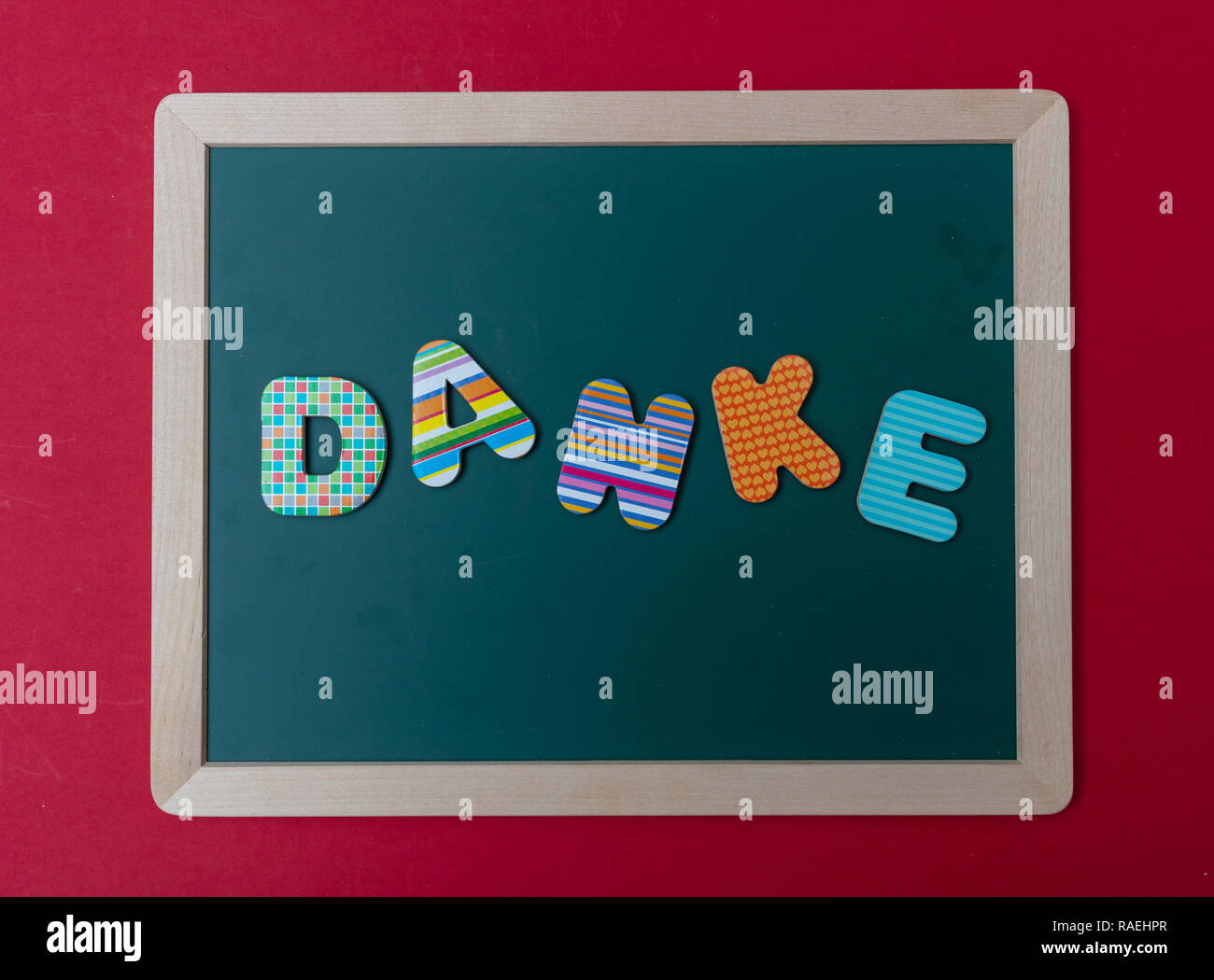 Danke, thank you, Colorful letters shaping the word Danke, thank you in german, on green board with wooden frame, red wall background Stock Photo