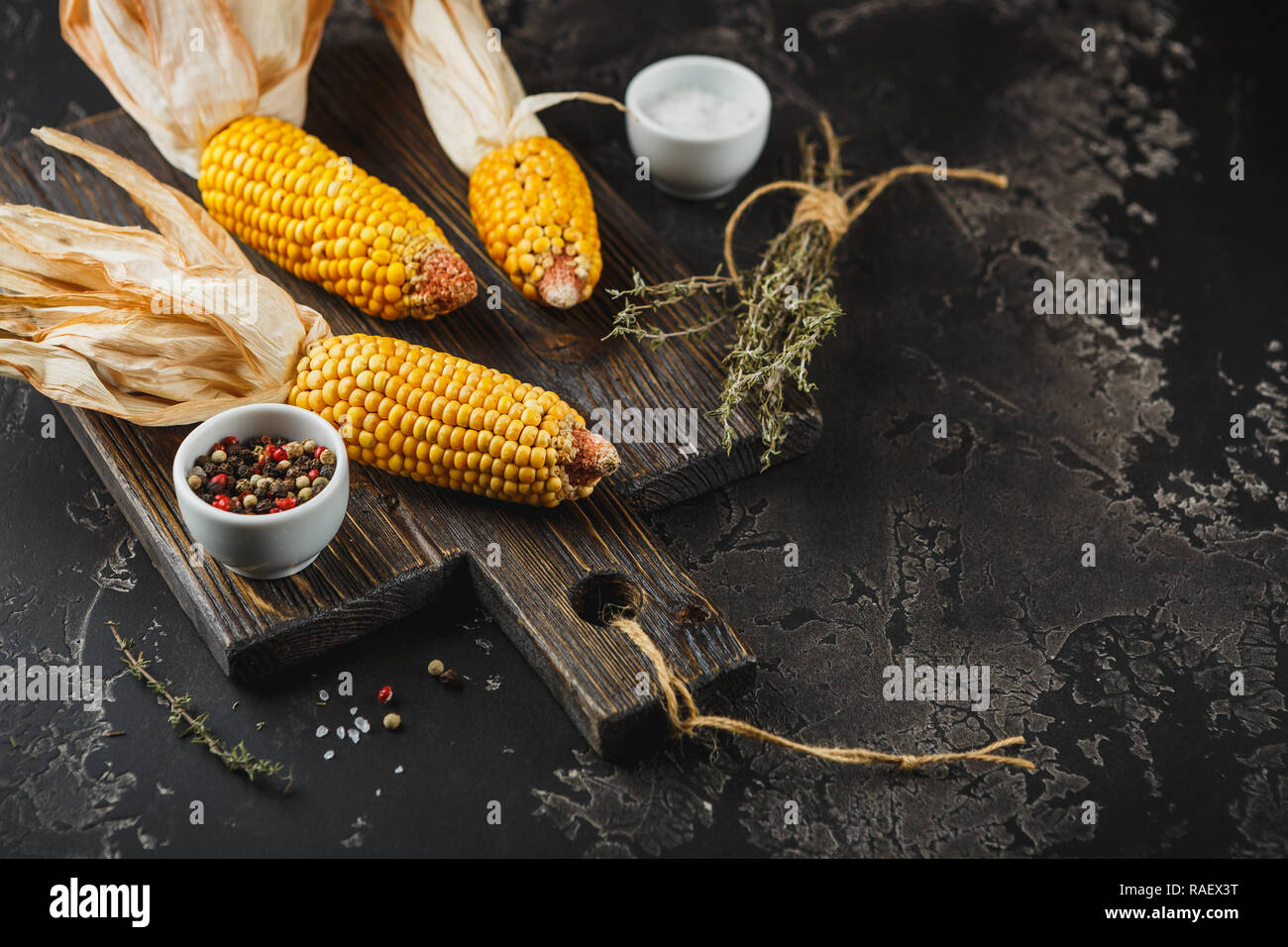 Yellow corn on cobs on grunge dark table, with Thyme, salt and pepper, closeup. Space for text. Stock Photo