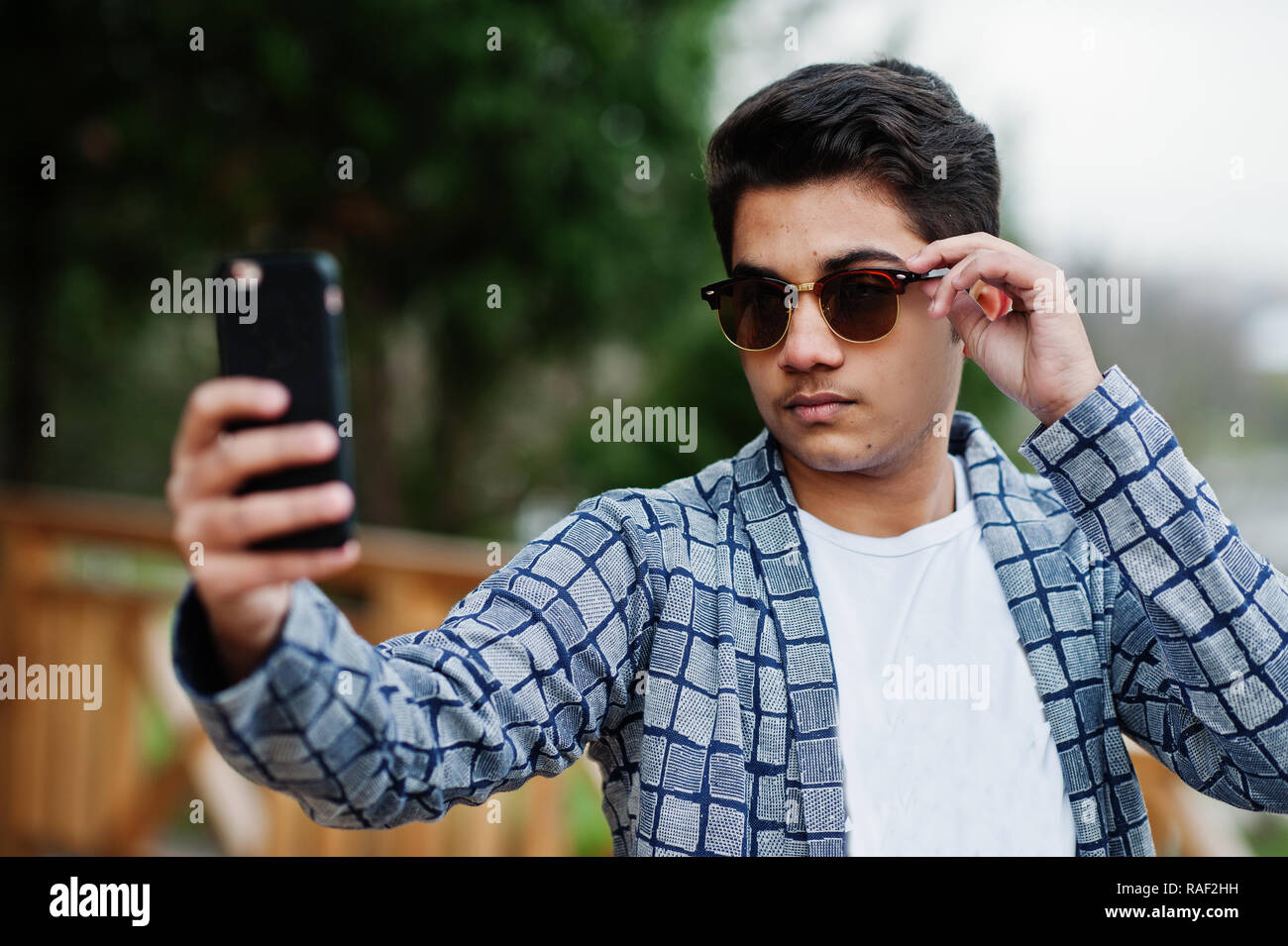 Stylish indian young man at sunglasses wear casual posed outdoor and making selfie at mobile phone. Stock Photo