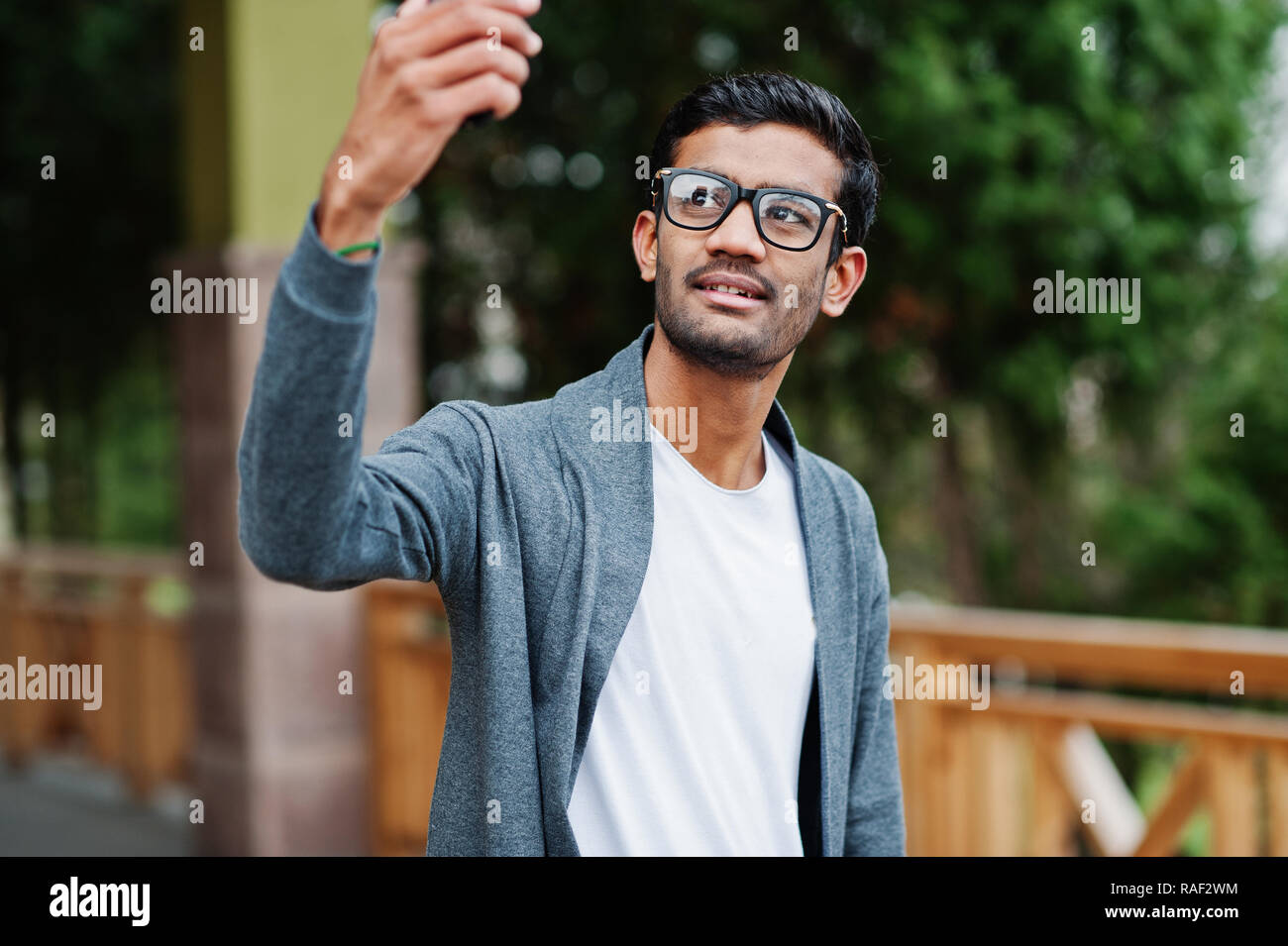 Casual young indian man in silver blazer and sunglasses posed against  wooden background, making selfie on phone Stock Photo - Alamy