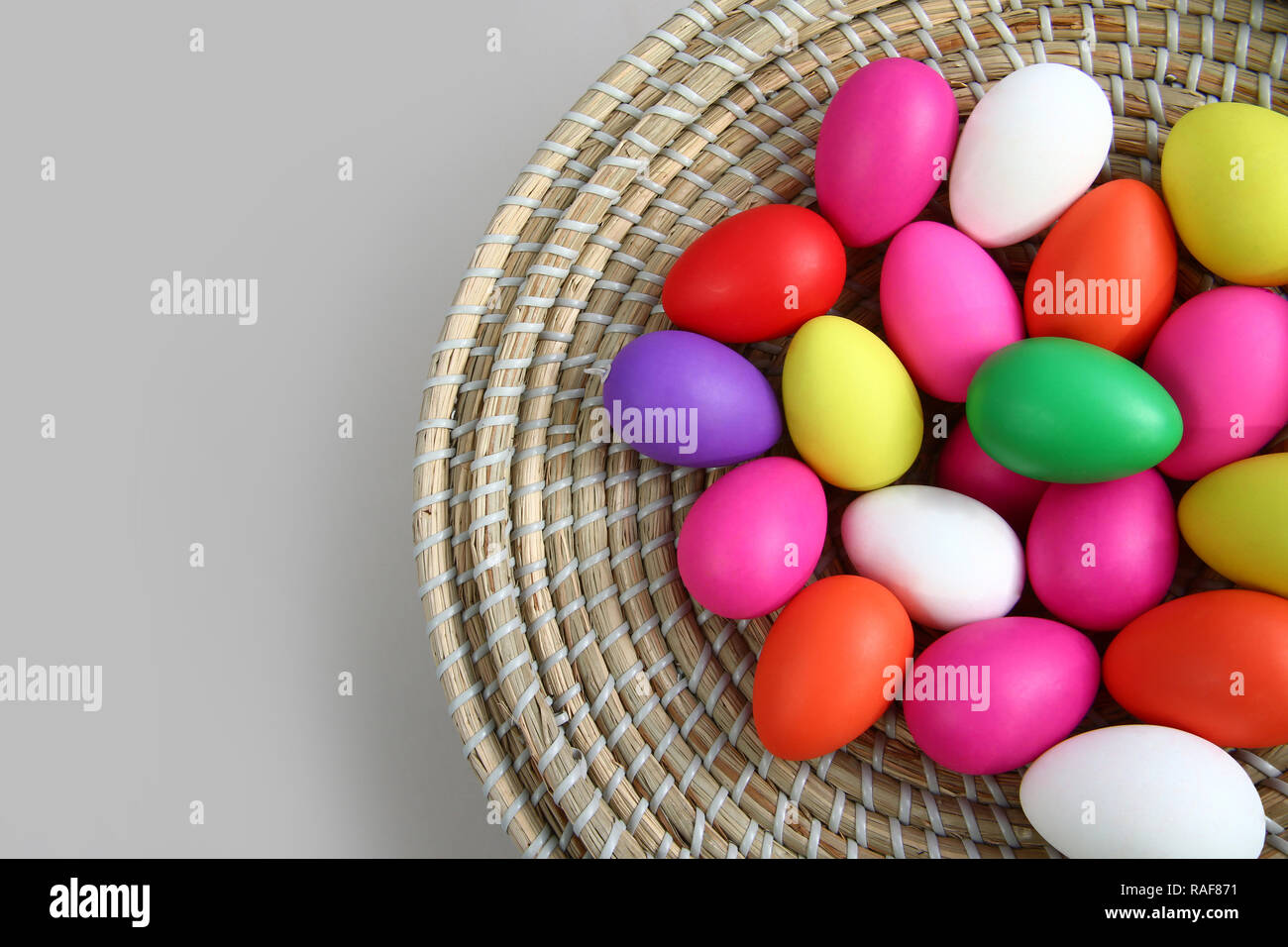 Brightly colored easter eggs, in a straw basket against a grey background. Stock Photo