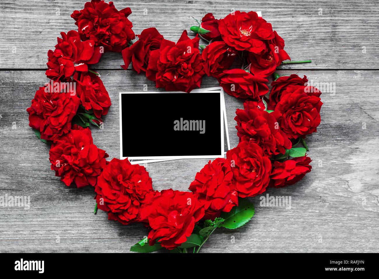 red rose flowers heart shaped with blank photo frame on rustic wooden background. Valentine day concept. top view. mock up Stock Photo