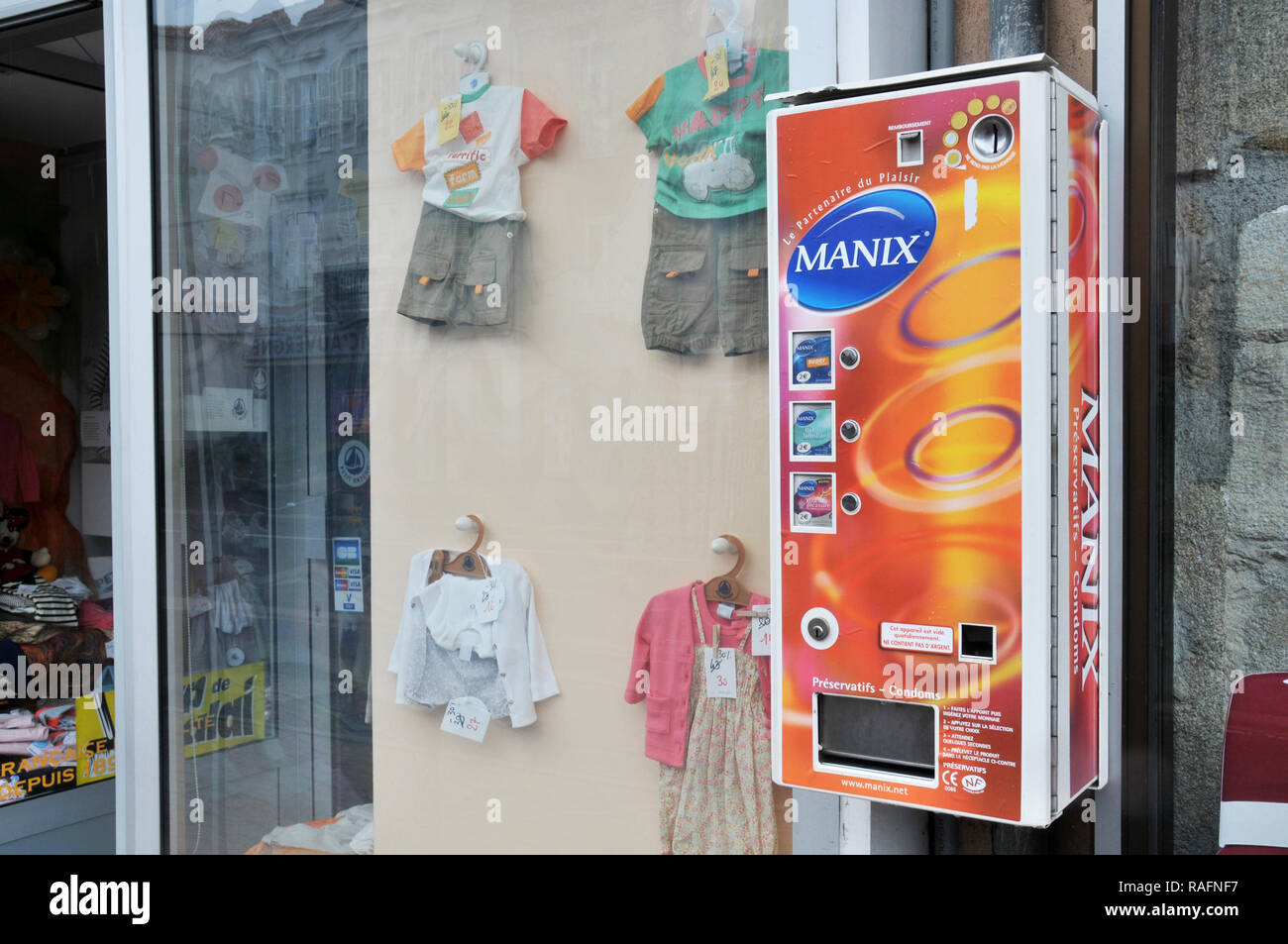 Distributor of condoms located next to a children's clothing store.Issoire, Auvergne, France Stock Photo