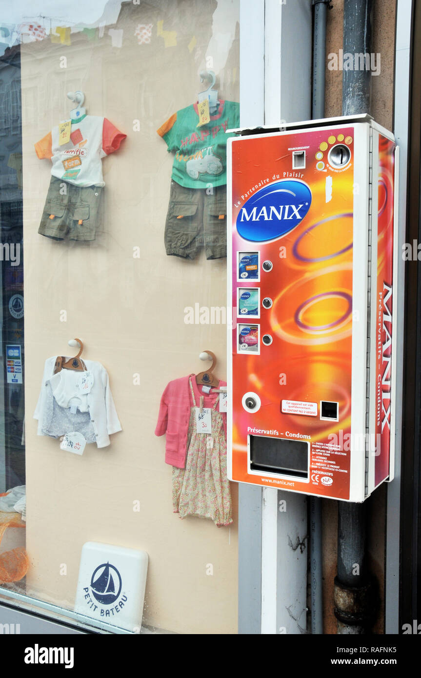 Distributor of condoms located next to a children's clothing store. Issoire, Auvergne, France.. Stock Photo