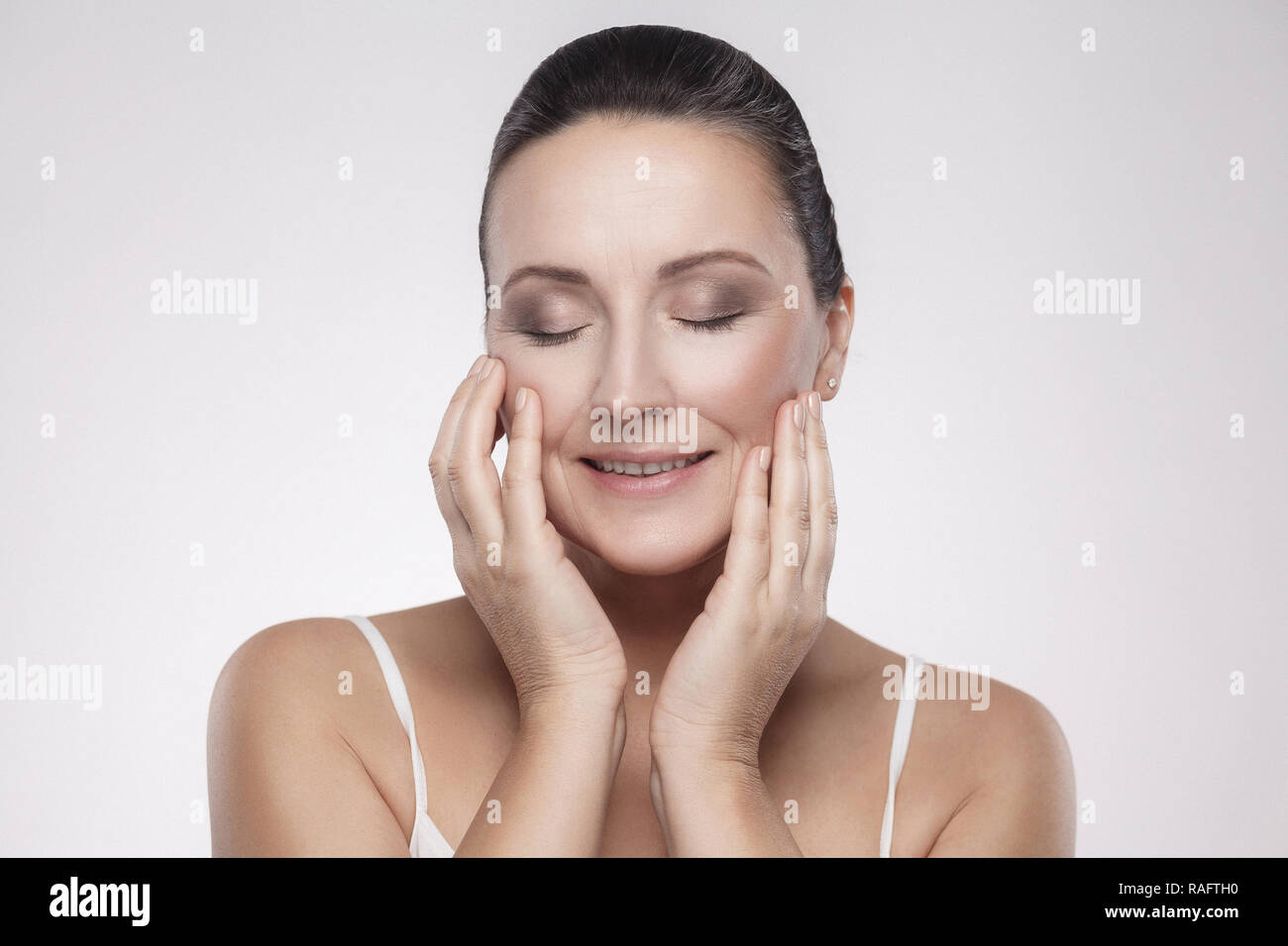 Portrait of happy smiling charming, beautiful woman touching skin or applying cream, with perfect skin after cream, balm, mask, lotion, isolated on gr Stock Photo