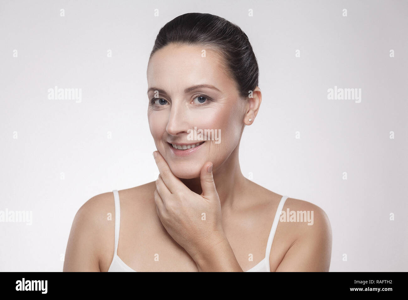 Closeup portrait of happy smiling charming, beautiful woman touching, enjoying her perfect face skin, holding fingers on cheek, dry, oiled, isolated o Stock Photo