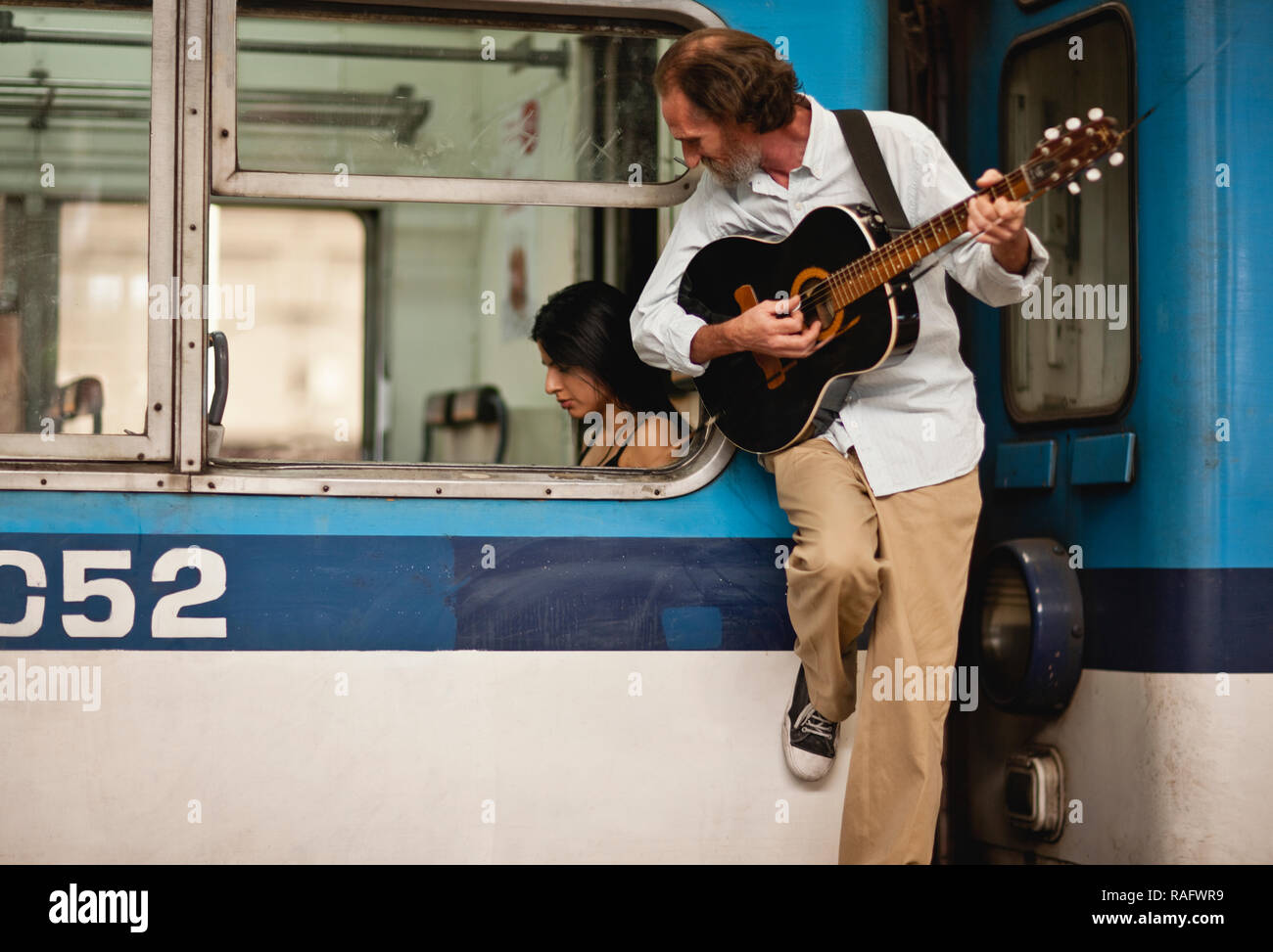 Man leaning on subway car playing guitar while checking out a female passenger. Stock Photo