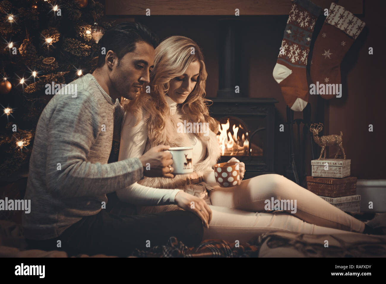Loving couple by a roaring log fire at Christmas drinking hot ...