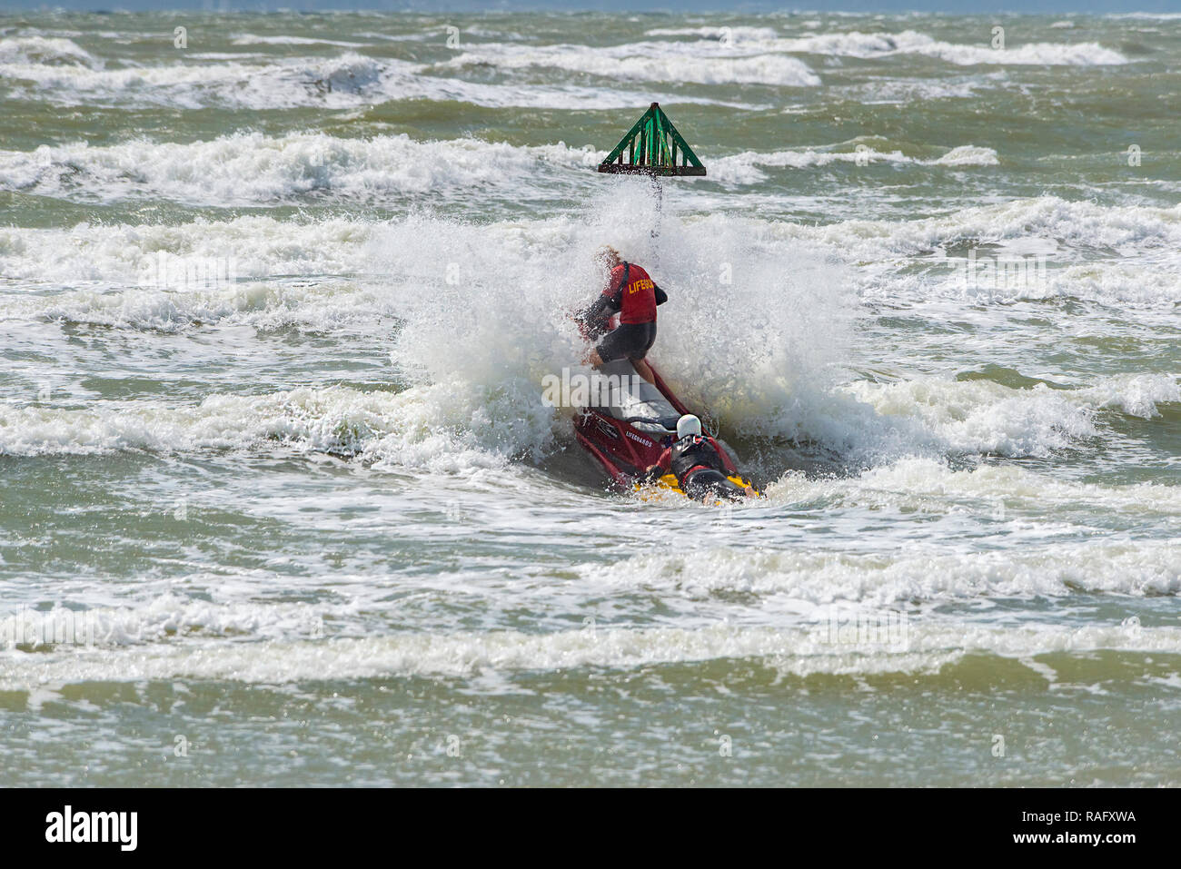 Two lifeguards hit a large wave as they enter the rough sea on a jetski or personal watercraft on West Wittering Beach, near Chichester,West Sussex,UK Stock Photo