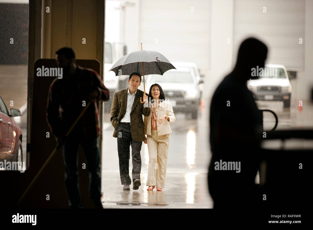 Businessman holding an umbrella for a colleague as they arrive at work. Stock Photo