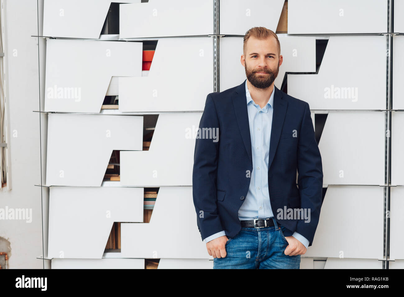 Stylish Bearded Young Man In Blazer And Jeans Standing Against Decorated Grey Wall With His Thumbs In Pockets Looking At Camera Half Length Front Po Stock Photo Alamy