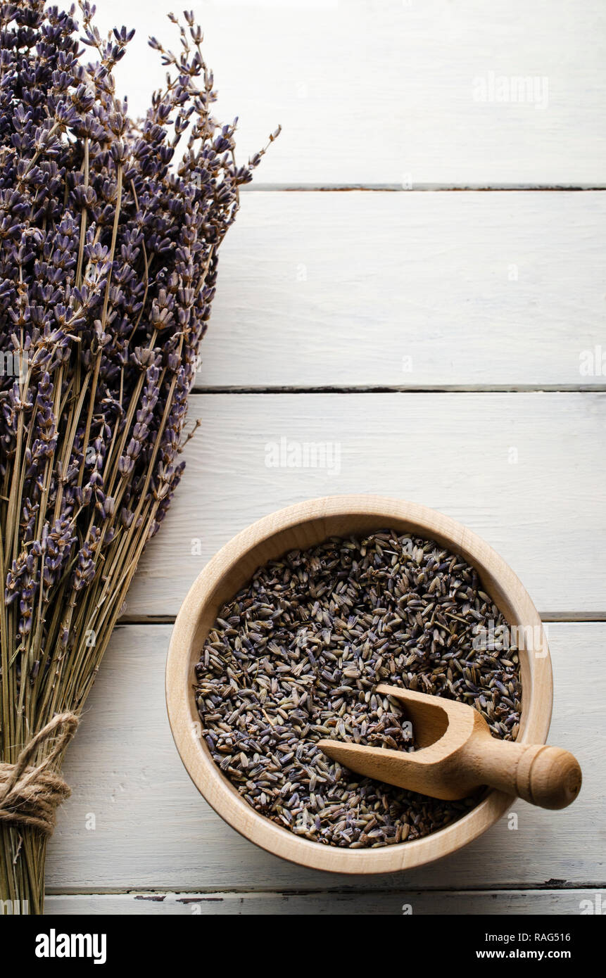 Overhead view of a tied lavender flower bunch next to a bowl of dried buds with wooden scoop on white planked table. Stock Photo
