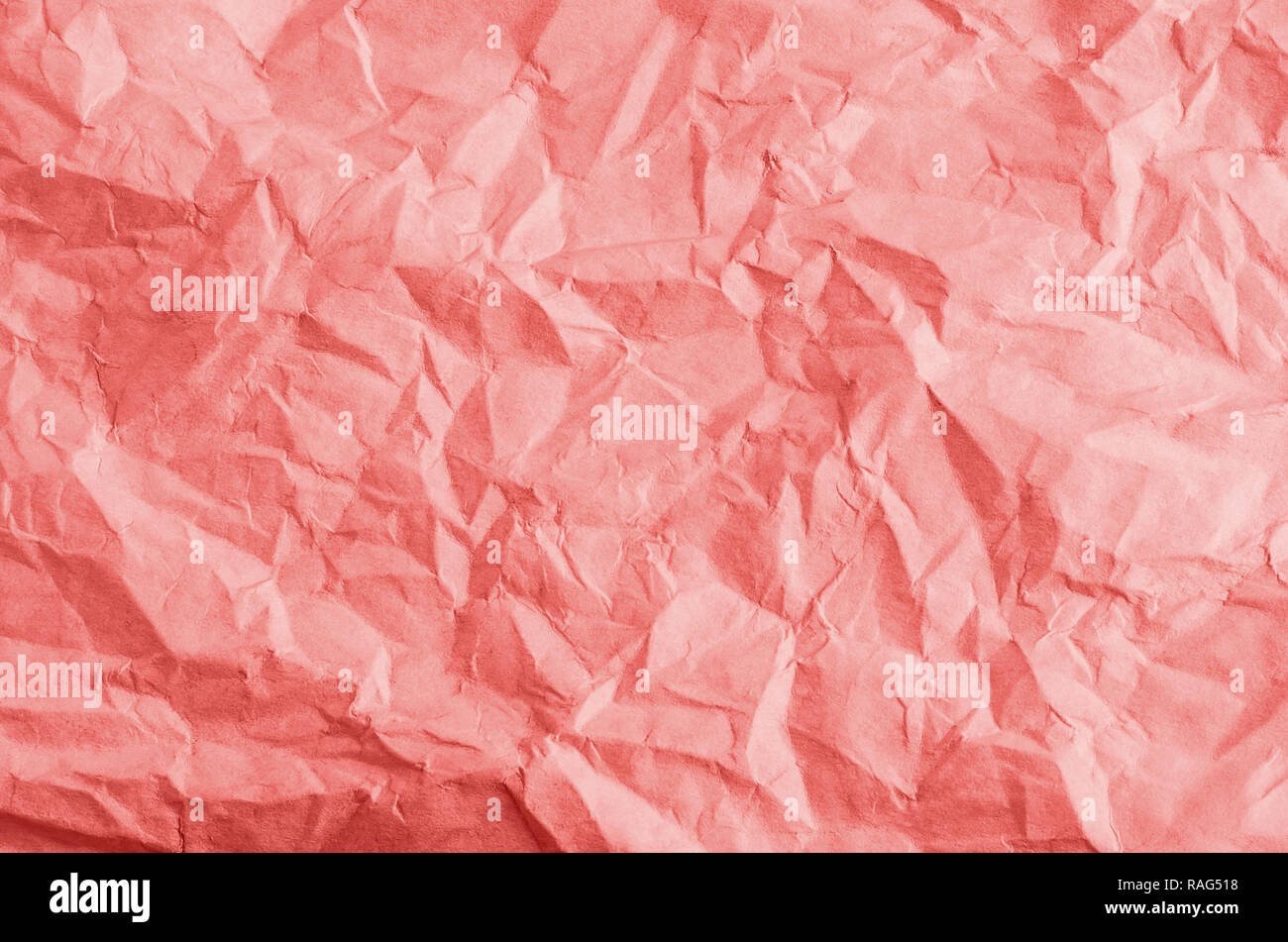 Crumpled, creased and unfolded paper background texture in a coral hue. Stock Photo