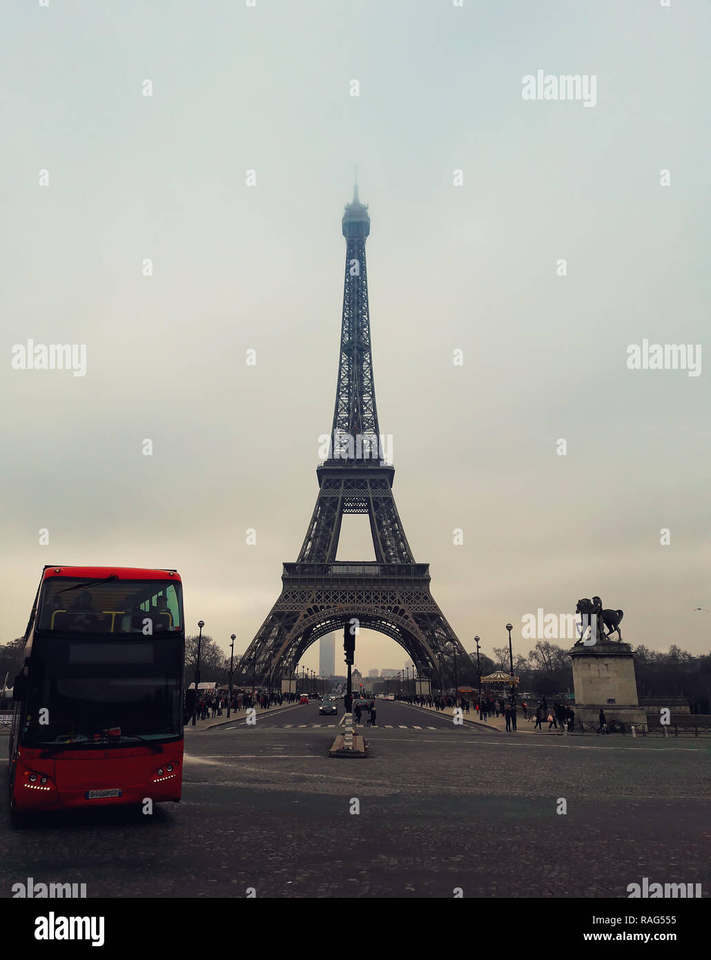 A red tourist bus on the pavement road in front of the famous Paris landmark Eiffel Tower view from the street. Stock Photo