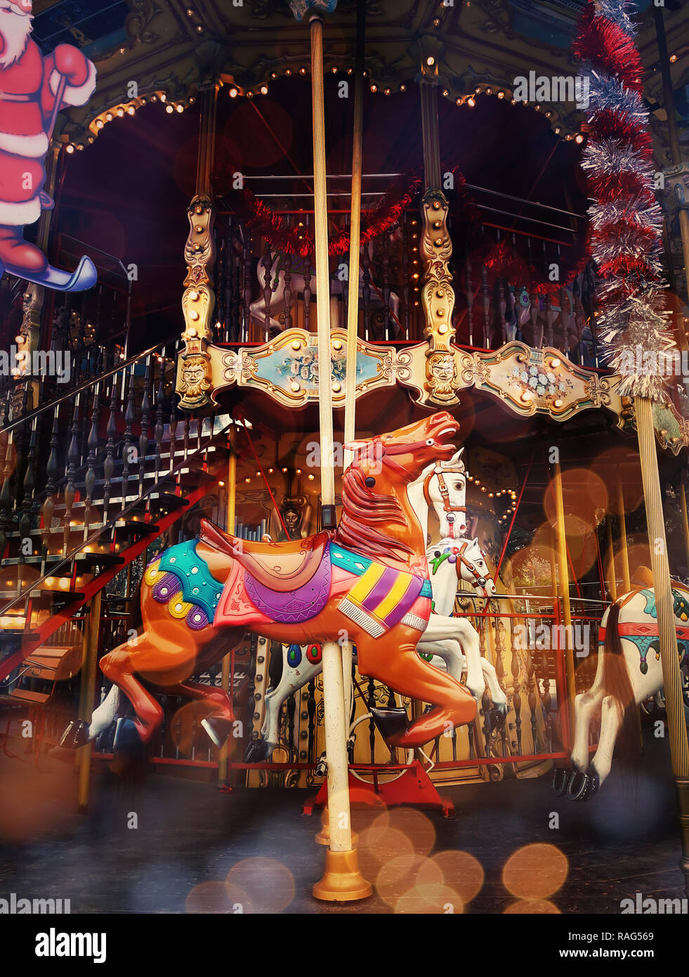 Beautiful bright children carousel in amusement park at night in winter. Close up up running horses silhouettes with vintage Christmas decorations, gl Stock Photo
