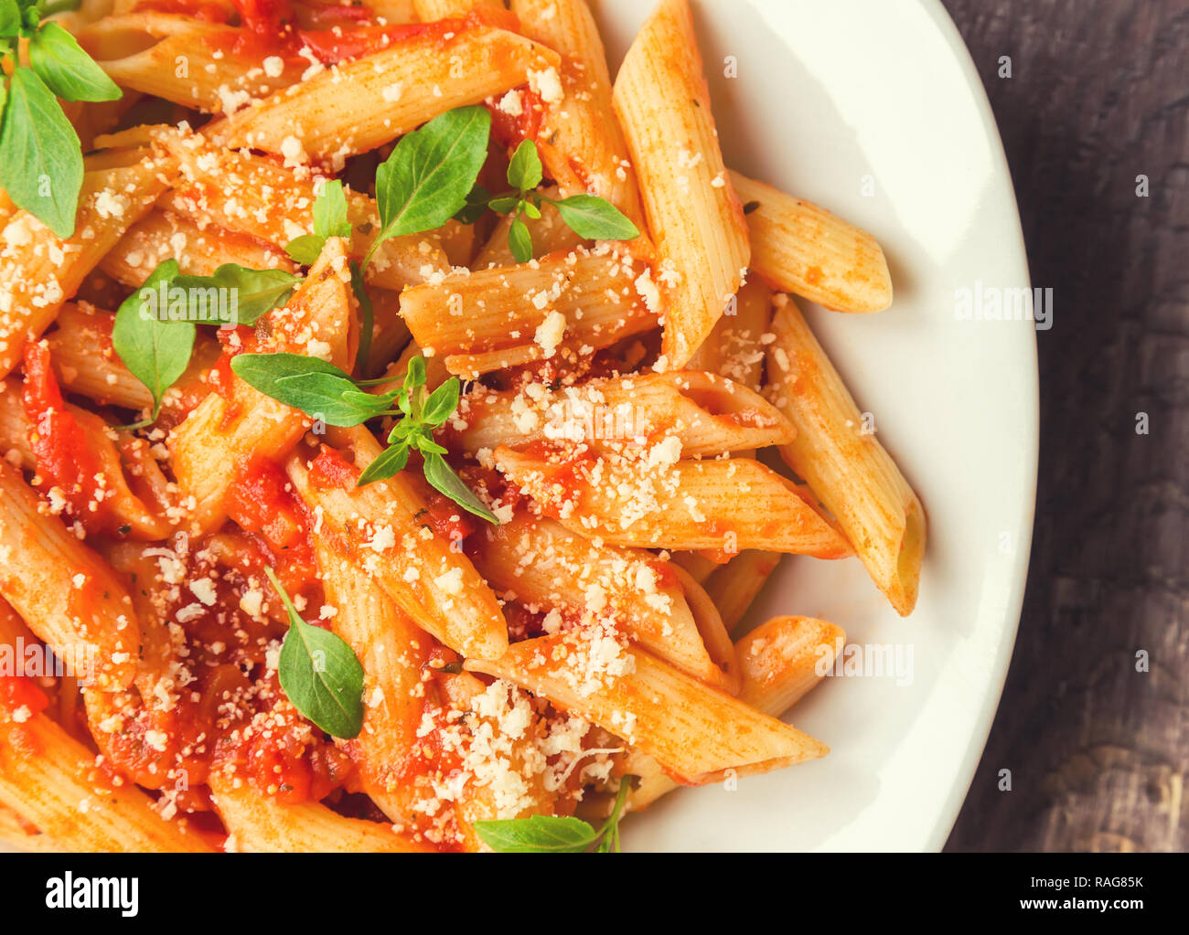 Penne pasta in tomato sauce with basil and parmesan cheese on rustic