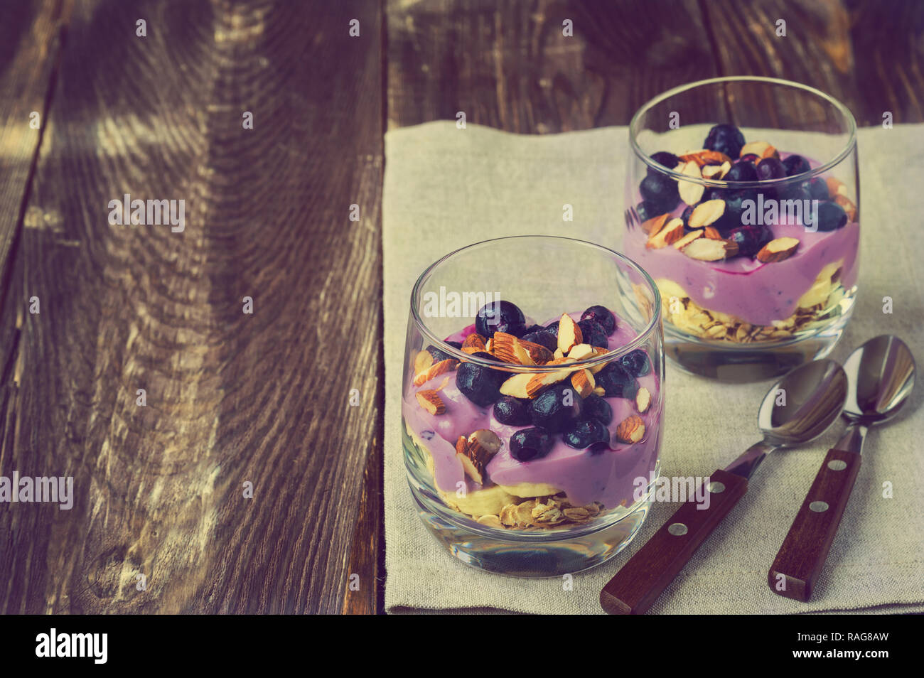 Dessert of oatmeal, banana, yogurt, blueberries and almond in glass bowls on rustic wooden background. Vintage toned picture. Stock Photo