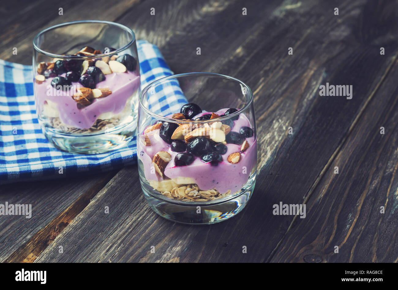 Dessert of oatmeal, banana, yogurt, blueberries and almond in glass bowls on rustic wooden background Stock Photo