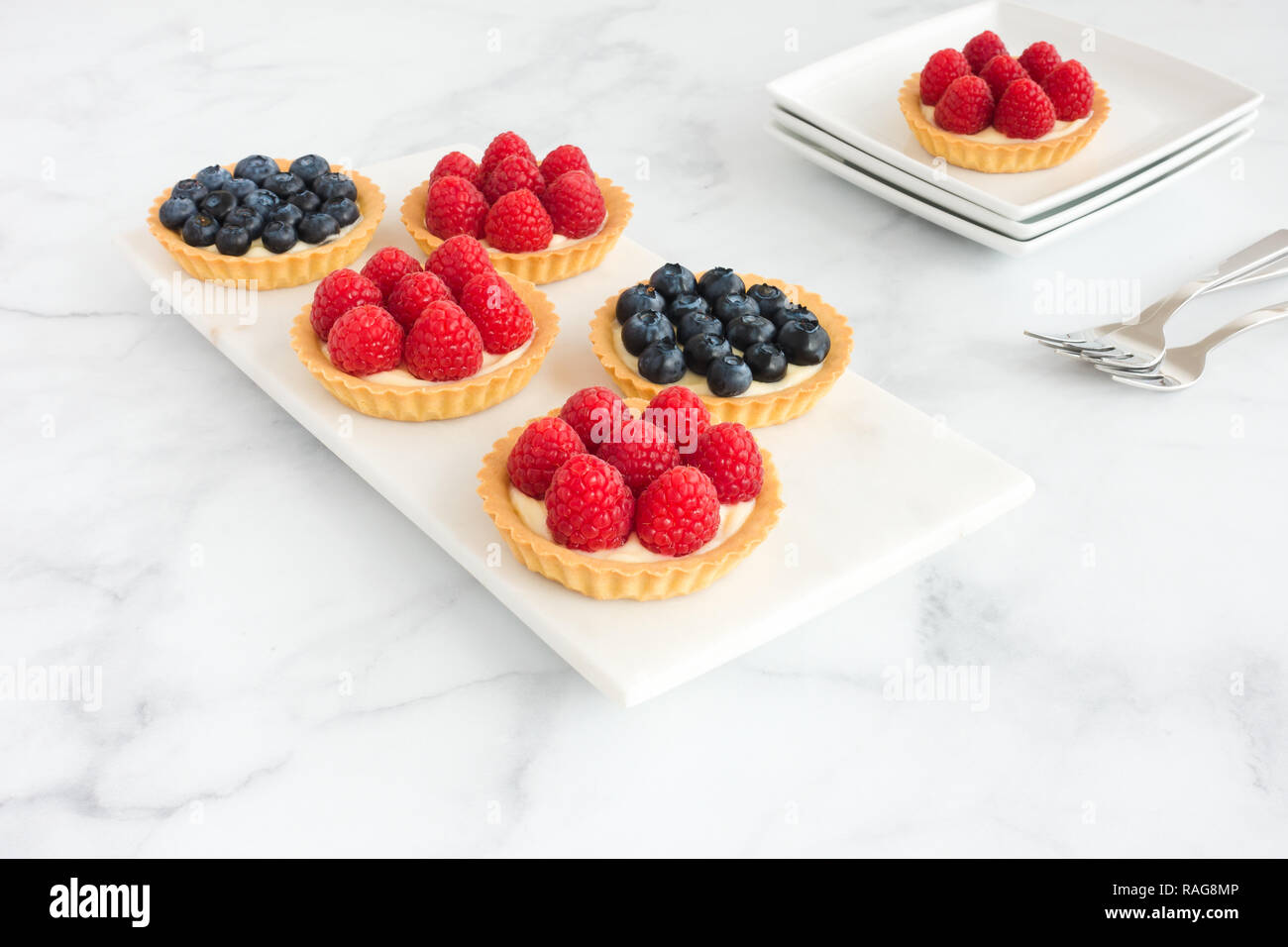 Homemade raspberry and blueberry tarts with a cream filling on white ...