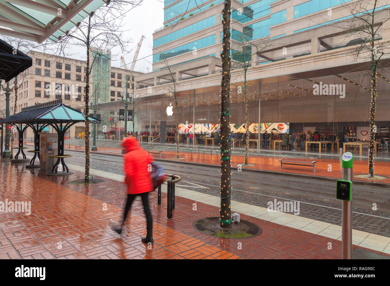 A pedestrian walk on the sidewalk during the rain, with the Apple Store