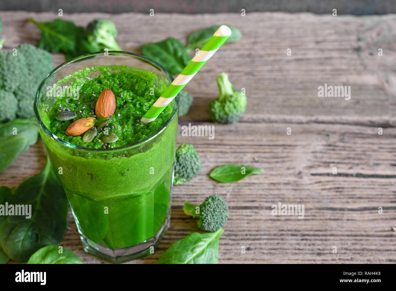 green healthy smoothie in a glass with broccoli, spinach, almonds and chia seeds over rustic wooden table. close up Stock Photo