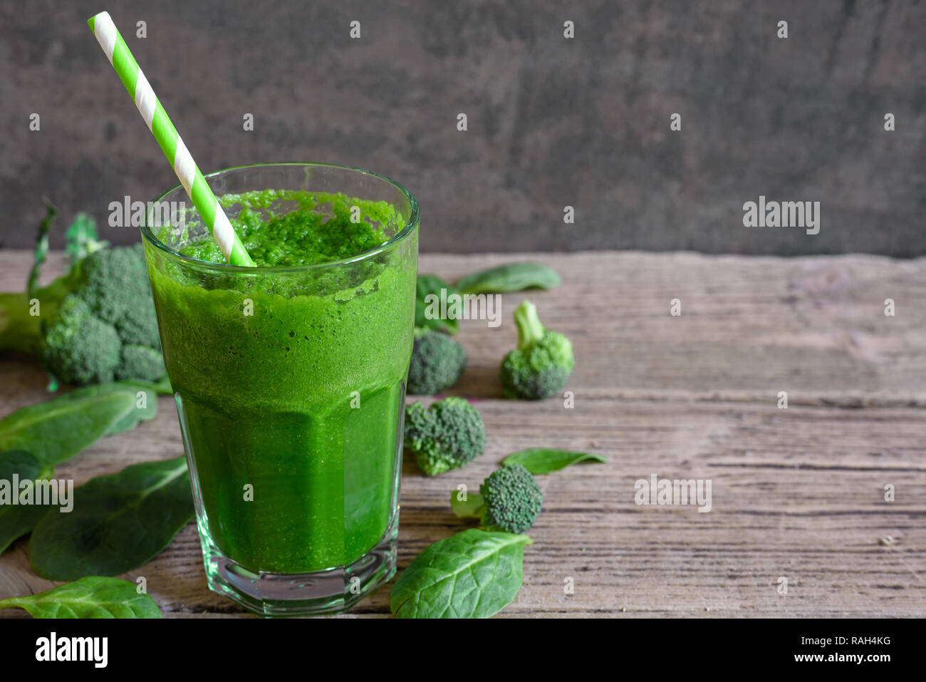 green healthy smoothie in a glass with broccoli, spinach and chia seeds with a straw over rustic wooden table. close up Stock Photo