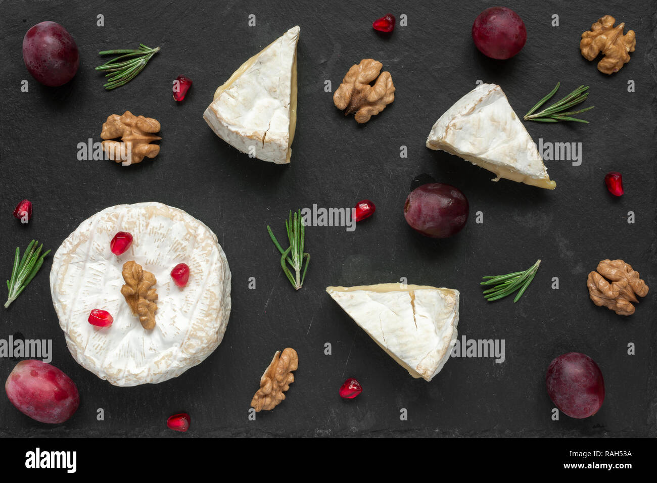composition of camembert or brie cheese with grapes, walnuts, pomegranate and of rosemary on black slate background. top view. Healthy breakfast Stock Photo